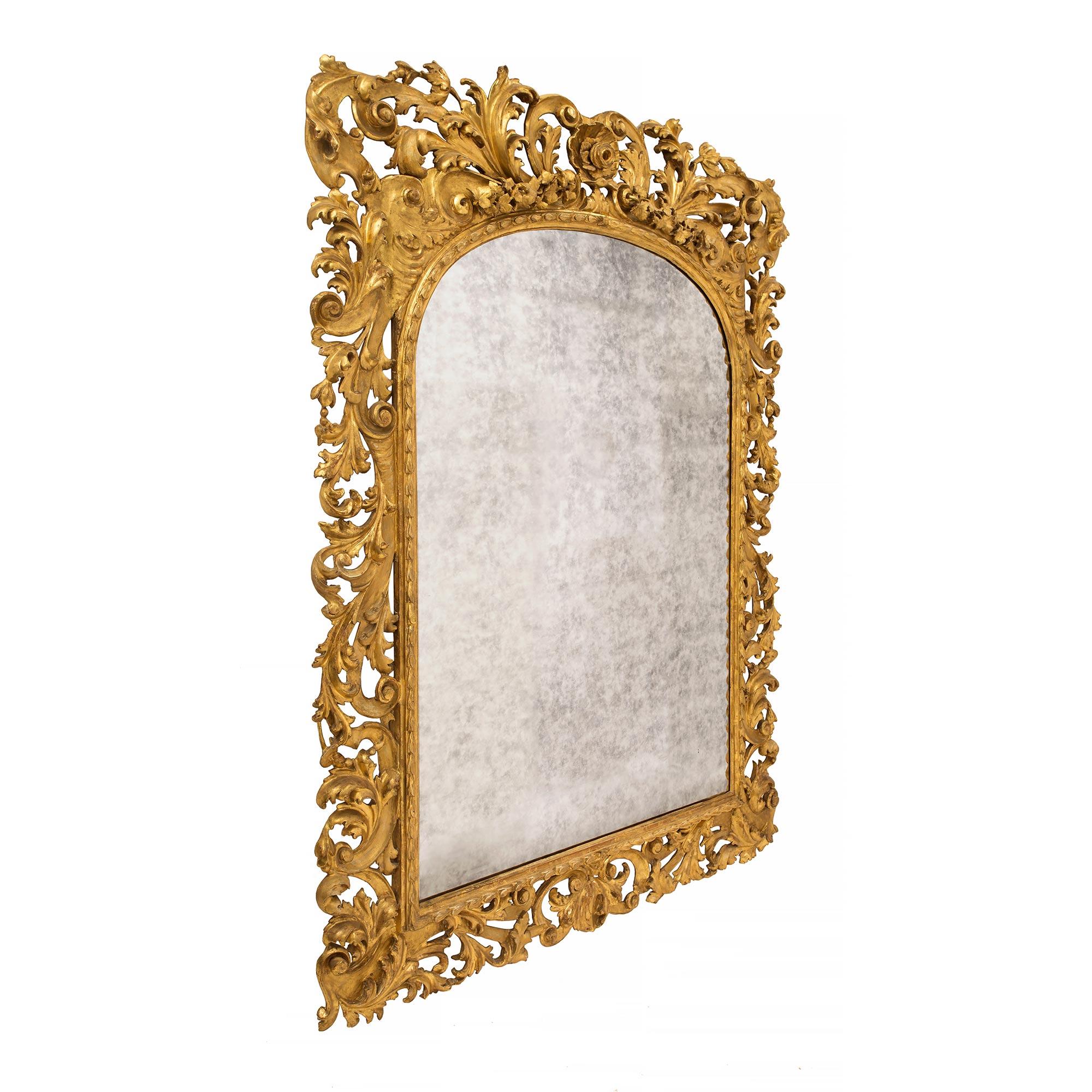 Un spectaculaire miroir baroque italien du milieu du XIXe siècle en bois doré. La plaque du miroir est entourée d'un cadre ajouré fortement et richement sculpté. Le cadre est orné de magnifiques volutes en 