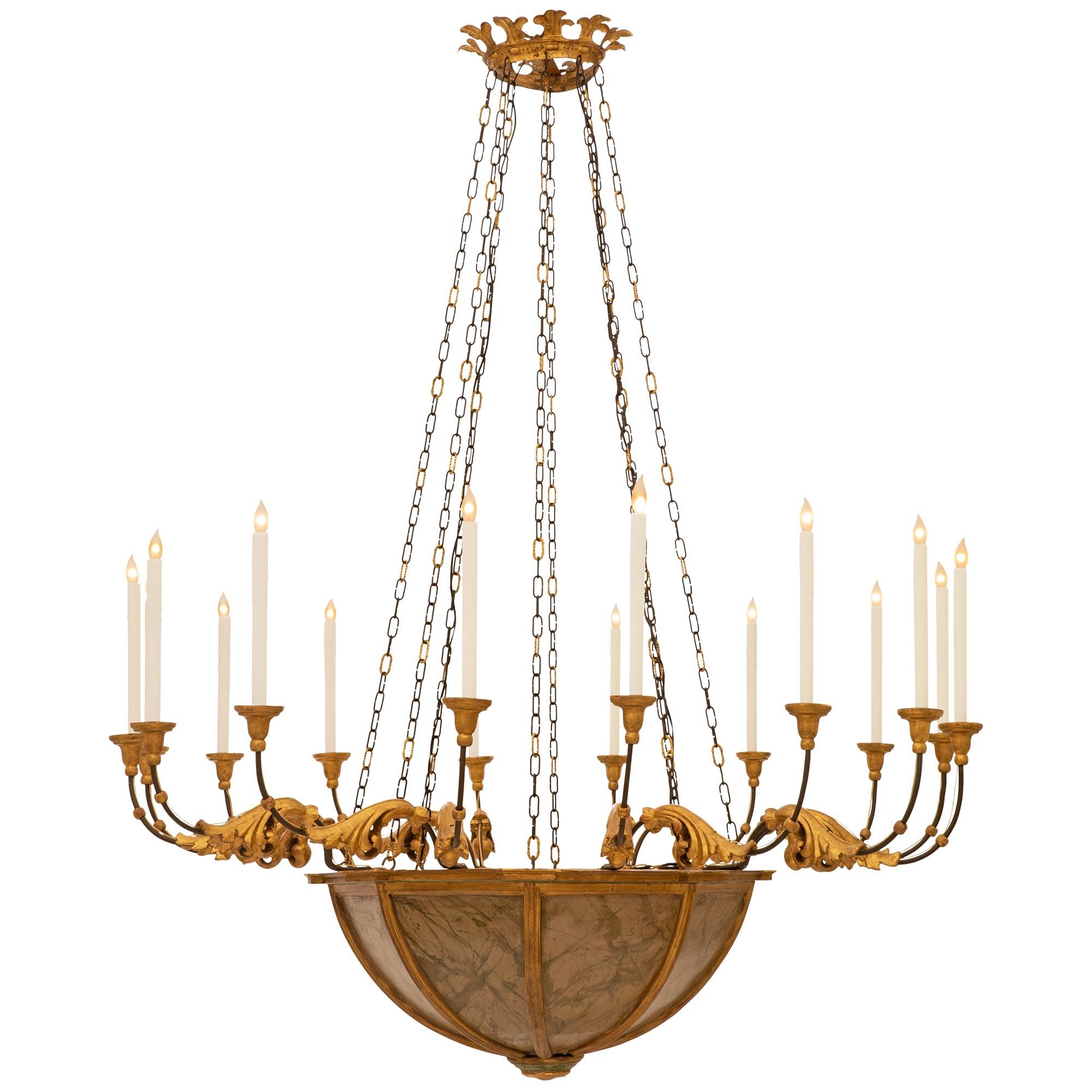 A large scale and elegantly detailed Italian 19th century Baroque st. Faux Painted marble, Giltwood, and Wrought Iron chandelier. This stately sixteen arm sixteen light chandelier is centered by a circular Giltwood and faux painted marble bottom
