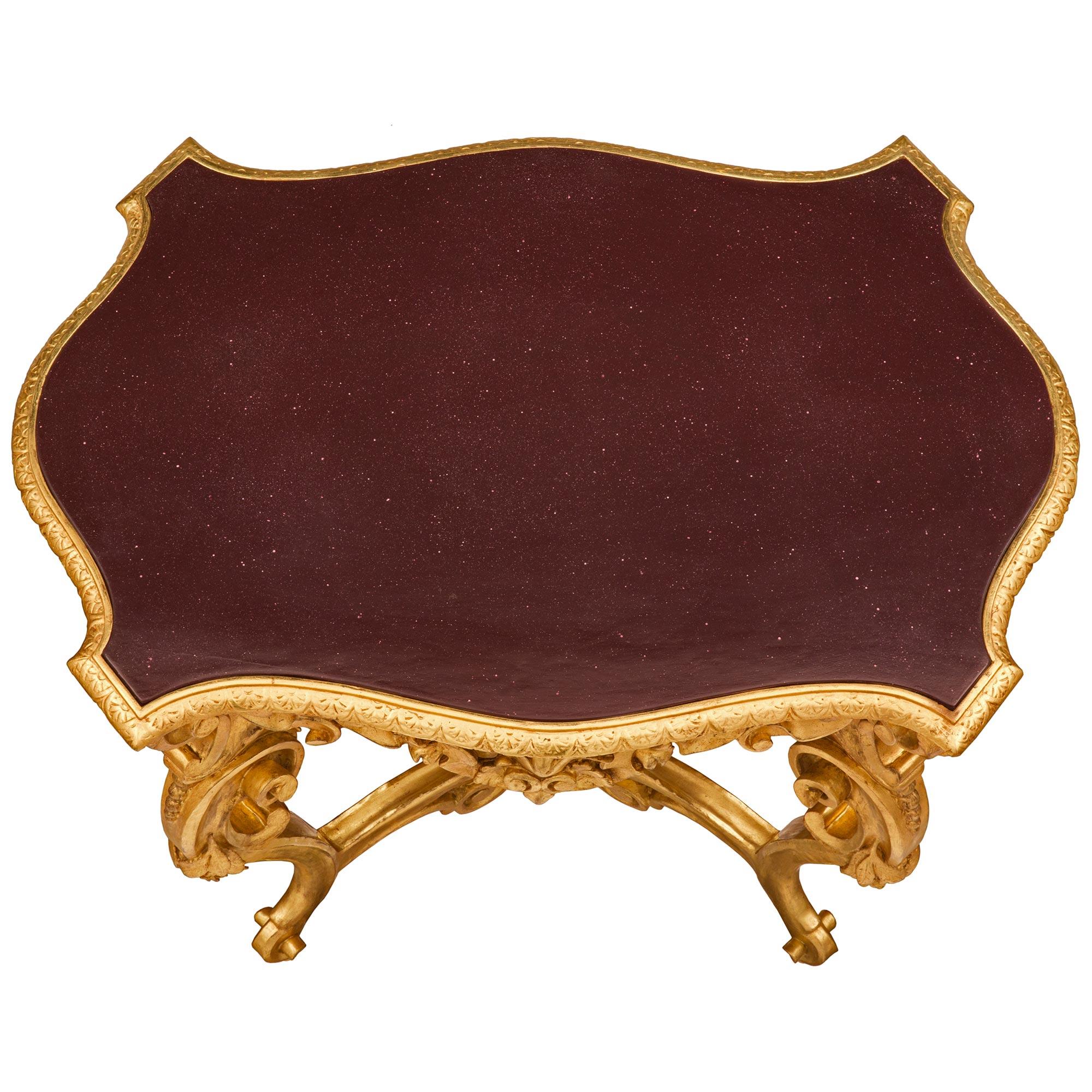 A stunning Italian 19th century Baroque st. giltwood and faux painted Porphyry center table. The oblong shaped table is raised by impressive and most decorative scrolled foliate legs adorned with charming finely detailed floral carvings. Each of the