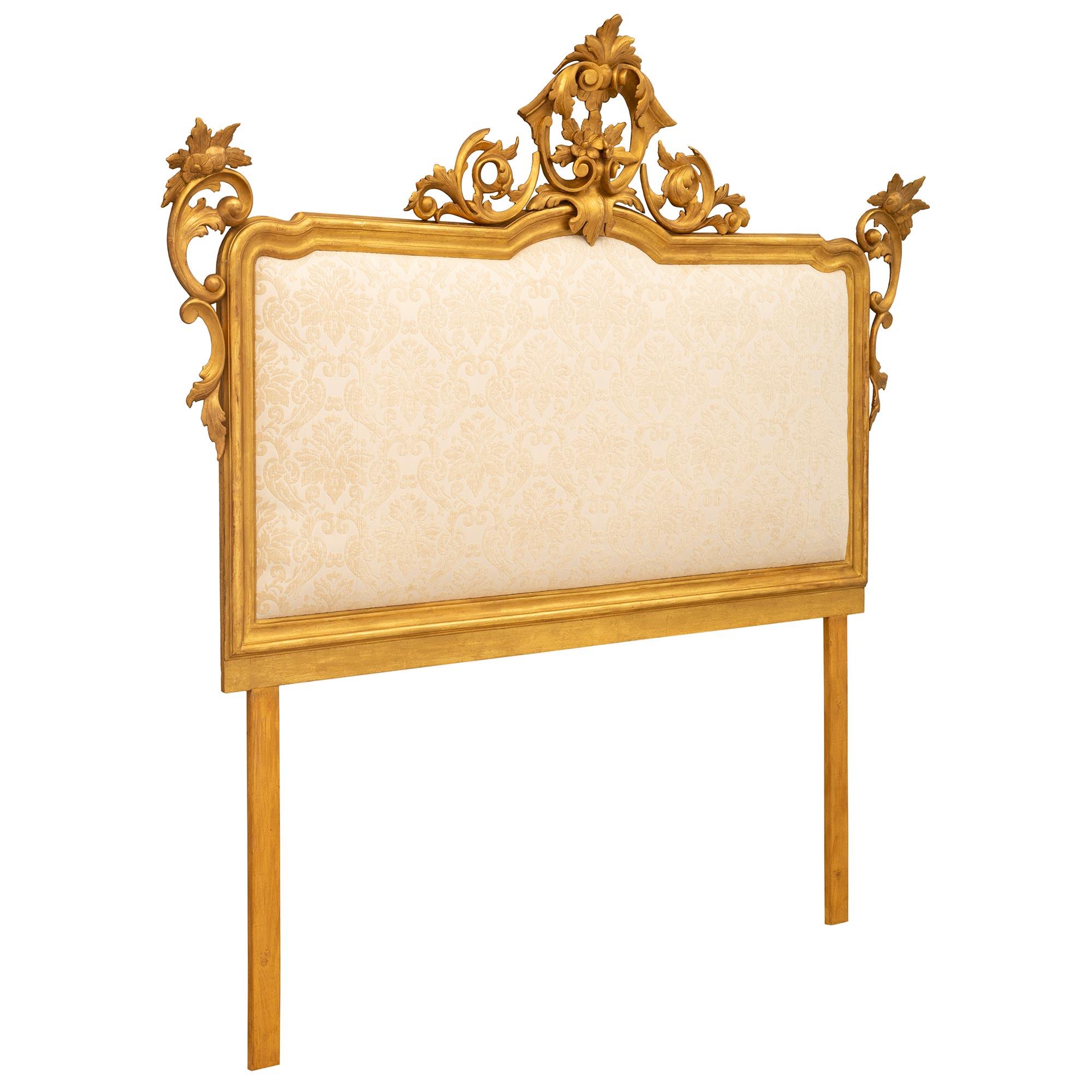 An exceptional Italian 19th century Baroque st. giltwood king sized upholstered head. The headboard is framed within an elegant wrap around mottled border with beautiful richly carved pierced scrolled foliate elements at each side. The striking
