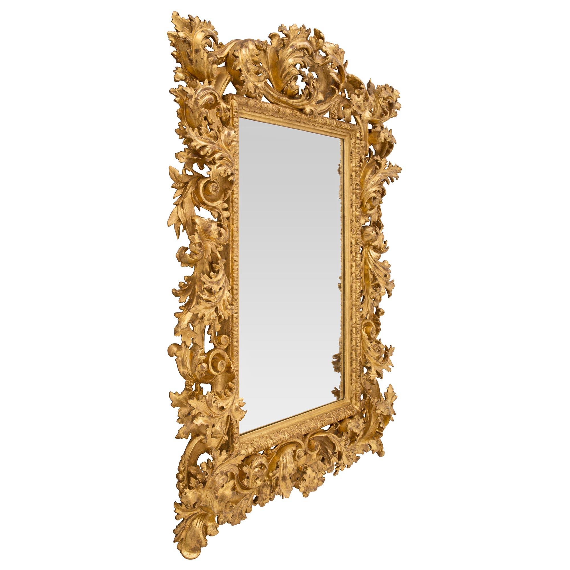 Impressionnant miroir baroque italien du 19ème siècle en bois doré. Le miroir est encadré d'une fine bordure droite tachetée avec une fine bande de feuillage enveloppante. Le cadre extérieur en bois massif présente une étonnante série de grandes