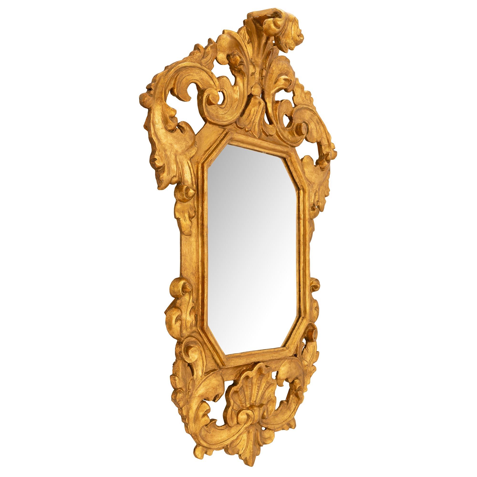 Merveilleux miroir baroque italien du 19ème siècle en bois doré. La plaque de miroir d'origine est encadrée dans une saisissante bordure en bois doré avec un grand cabochon de coquillage en bas, flanqué de mouvements de feuillage défilant sur le