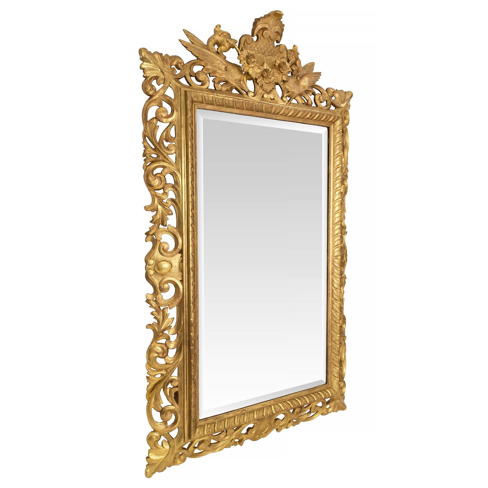 Exceptionnel miroir baroque italien du 19ème siècle en bois doré. La plaque de miroir biseautée d'origine est encadrée dans un motif cannelé très décoratif. S'étendant le long de la base et sur chaque côté, de riches mouvements sculptés de volutes