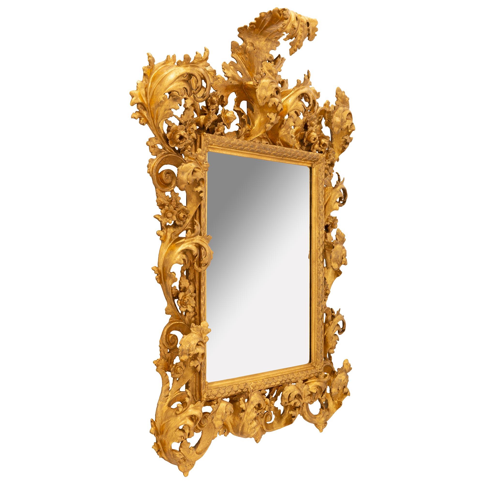 Un impressionnant et très décoratif miroir baroque italien du 19ème siècle en bois doré. La plaque de miroir est sertie d'une fine bande mouchetée avec un joli motif superposé en forme d'écaille de poisson. Le cadre extérieur présente de superbes