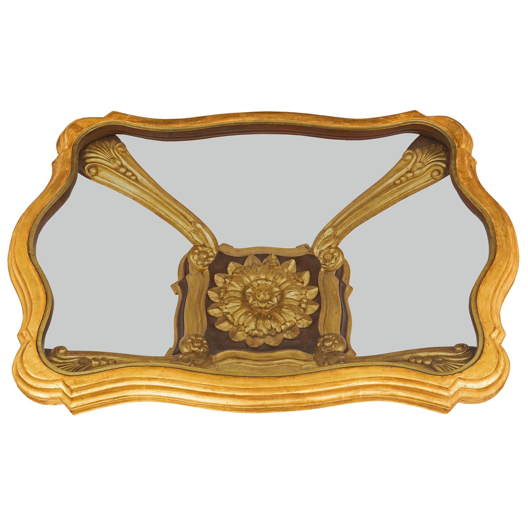 Une belle et extrêmement décorative table basse baroque italienne du début du 19ème siècle en bois doré, polychrome et verre. La table est surélevée par une base élégamment incurvée avec un superbe motif marbré en escalier et une belle bande