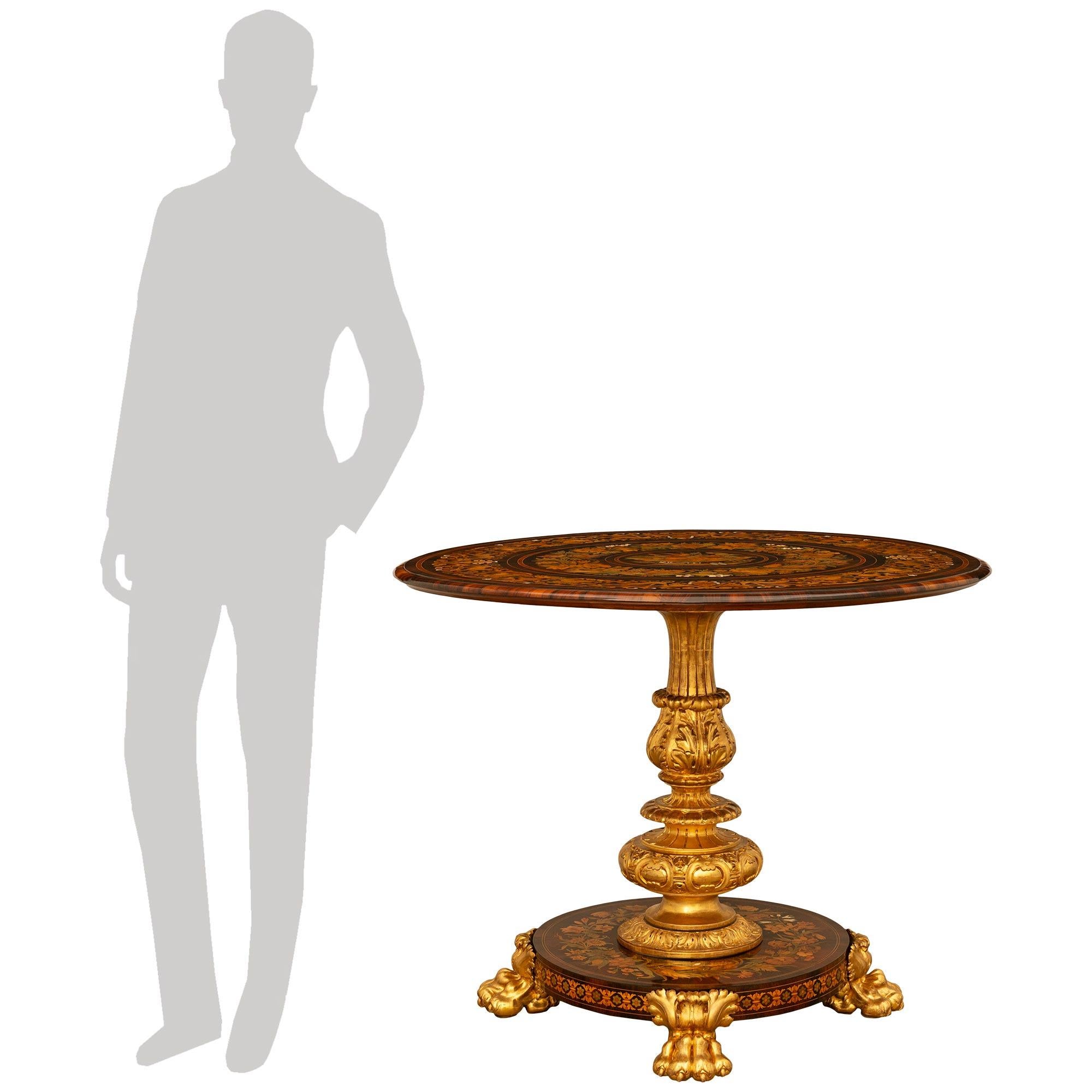 A stunning and high quality Italian 19th century Baroque st. Mahogany, Fruitwood and Giltwood tilt top center table. This intricately detailed table is raised on four Giltwood paw feet supporting a sumptuously inlaid circular base displaying
