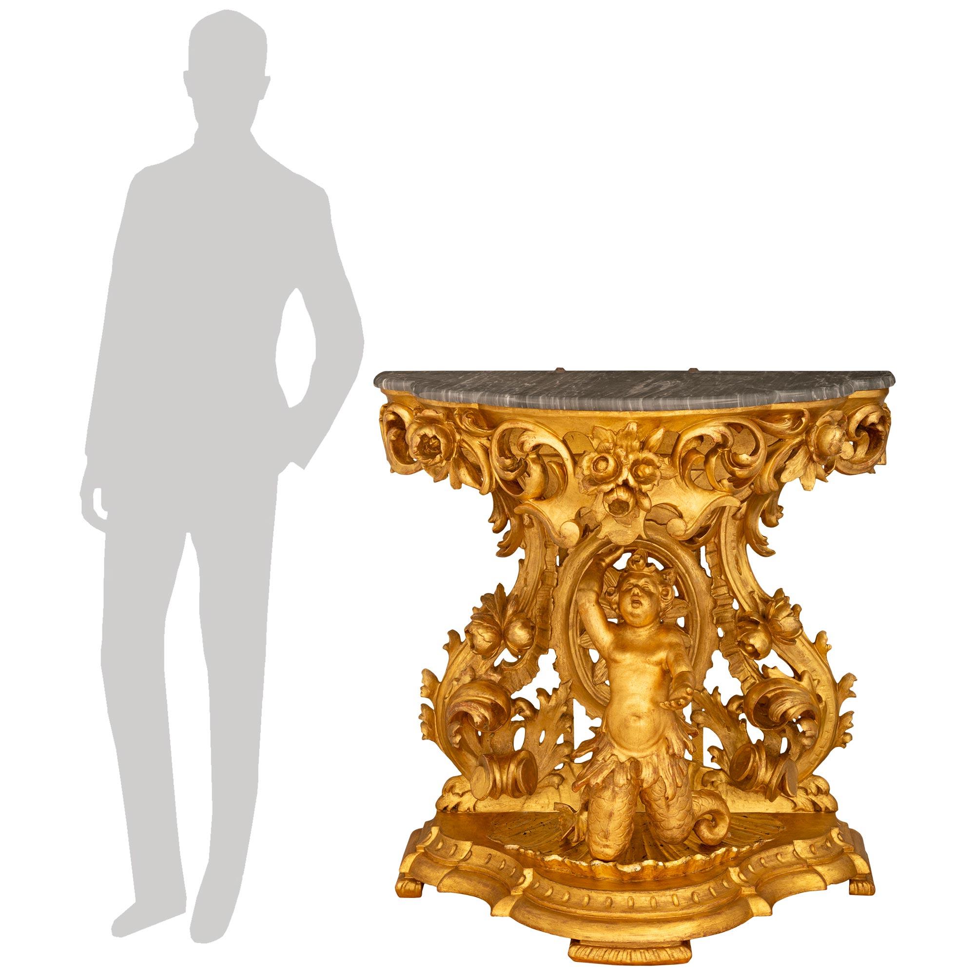 Una consola barroca italiana de principios del siglo XIX, muy decorativa y de gran calidad, de madera de meca, giltwood y mármol gris de Santa Ana. Esta consola de intrincada talla se eleva sobre una base moteada en forma de festón con tallas