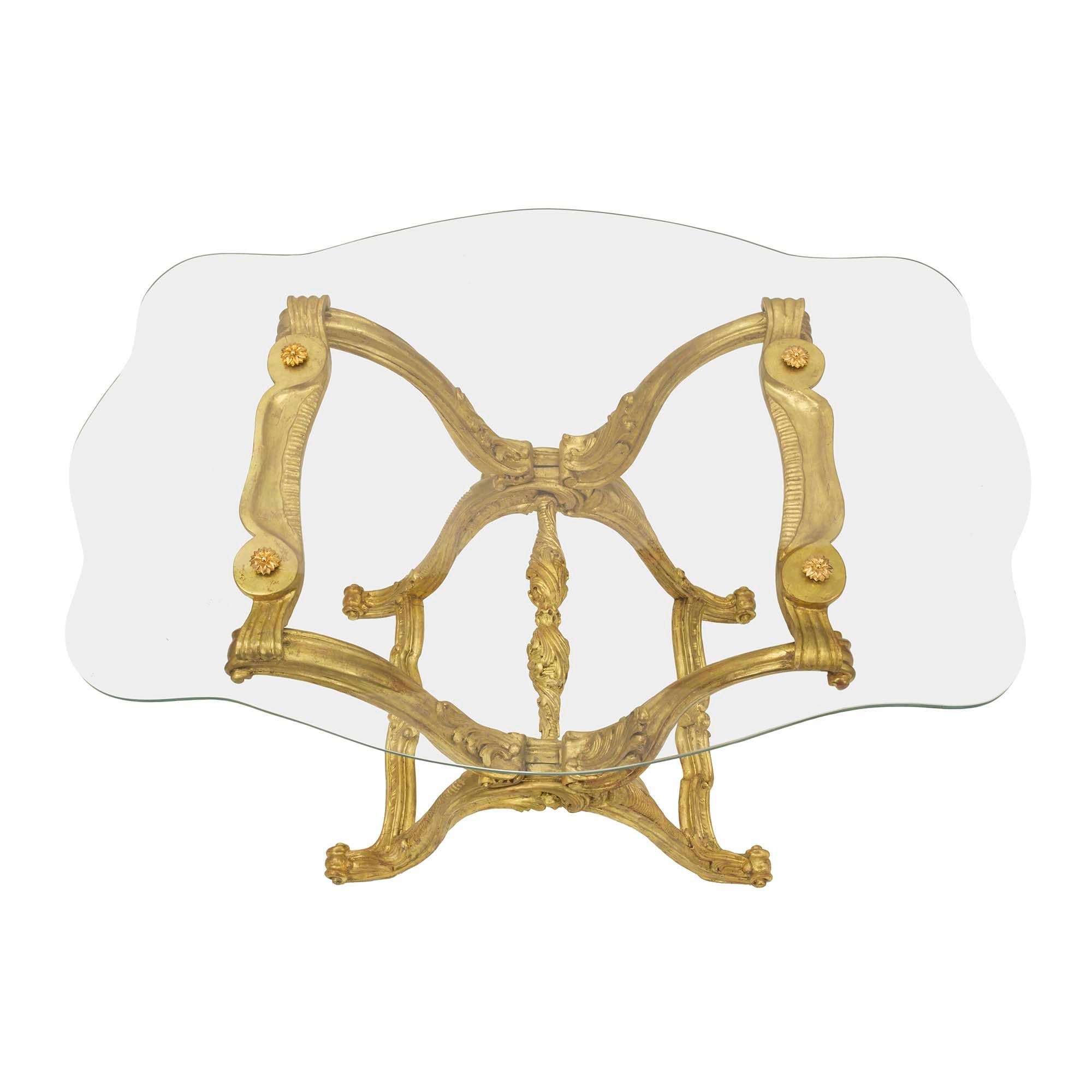 Ein sehr dekorativer und einzigartiger italienischer Cocktailtisch im Barockstil des 19. Jahrhunderts aus Goldholz und Glas. Der Tisch wird von reich geschnitzten X-förmigen Stützen mit auffallend geschwungenen Bewegungen und detailliert