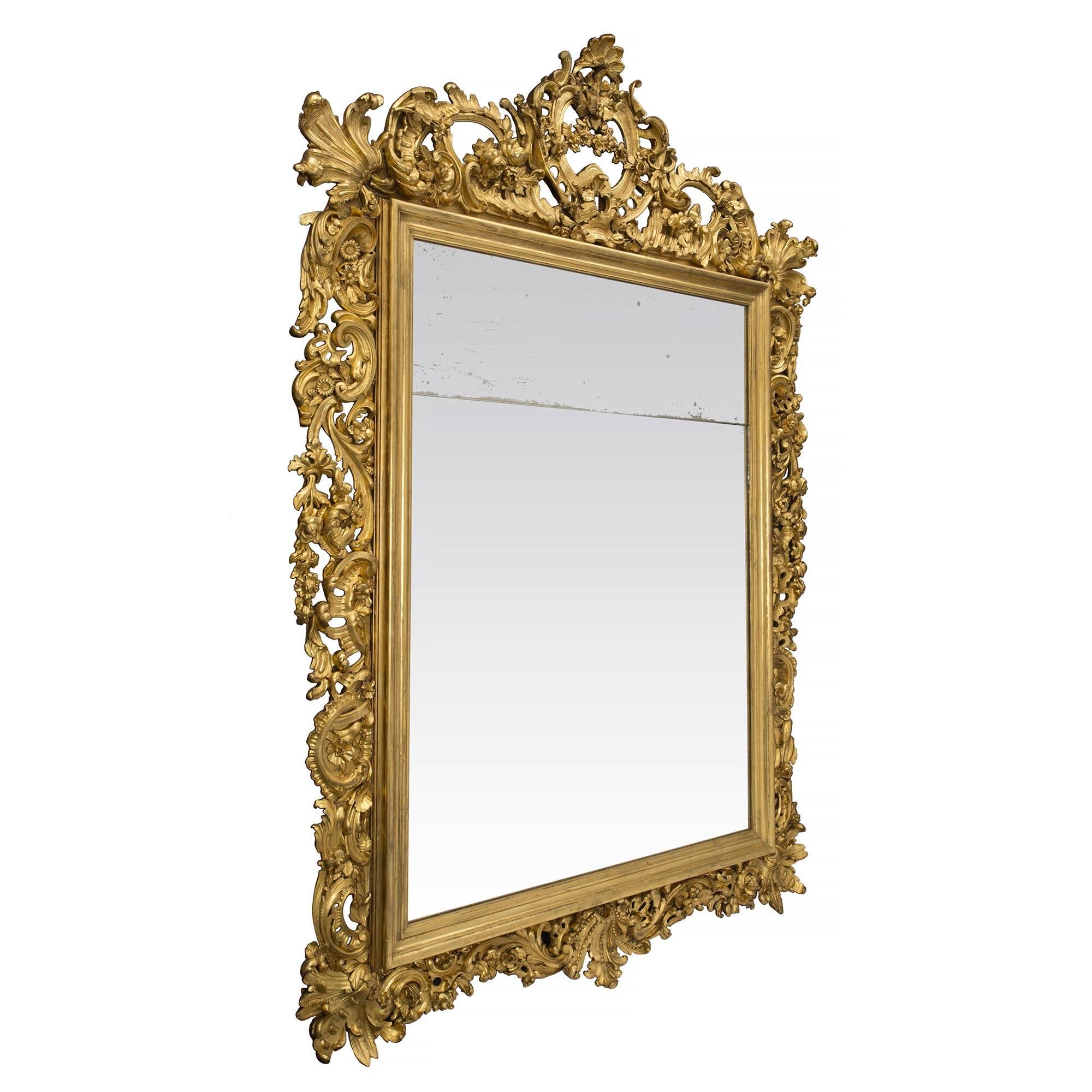 A most impressive and large scale Italian 19th century Baroque style giltwood mirror. The original rectangular mirror plate is framed within a fine mottled giltwood border. Extending throughout the frame are sensational and richly detailed carvings