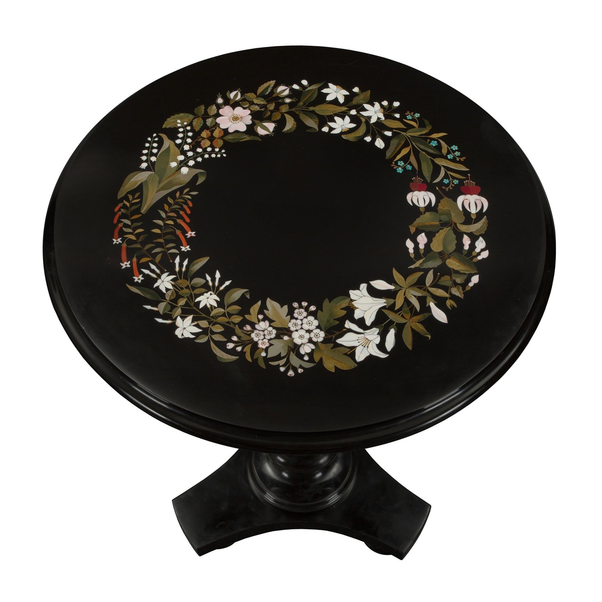 A striking Italian 19th century Black Belgian marble and Pietra Dura side table. The table is raised by a triangular base with concave sides and bun feet. The circular central support displays a most attractive carved turned design while the