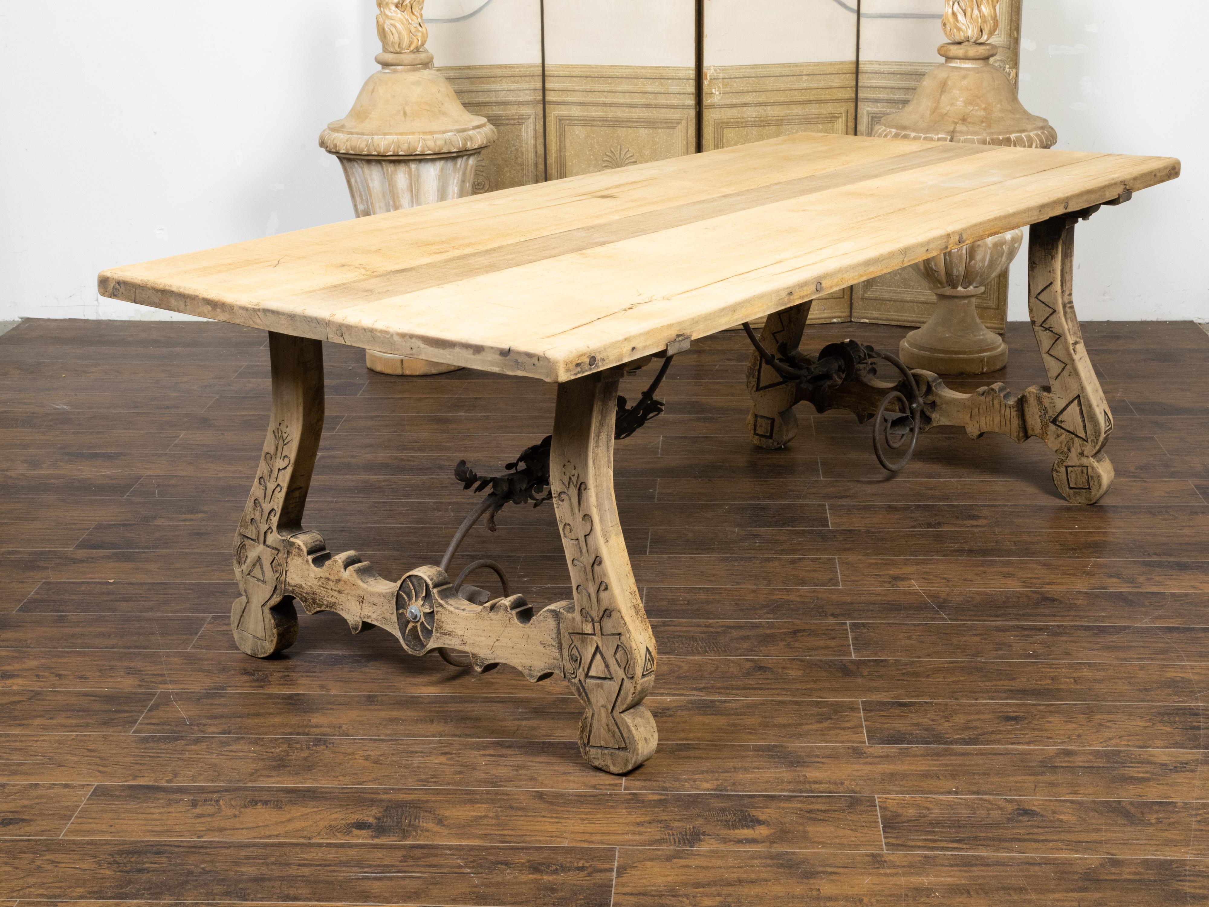 An Italian bleached oak farm table from the 19th century, with Baroque style base, incised carved floral and geometric décor and wrought iron scrolling stretchers. Created in Italy during the 19th century, this farm table features a bleached oak