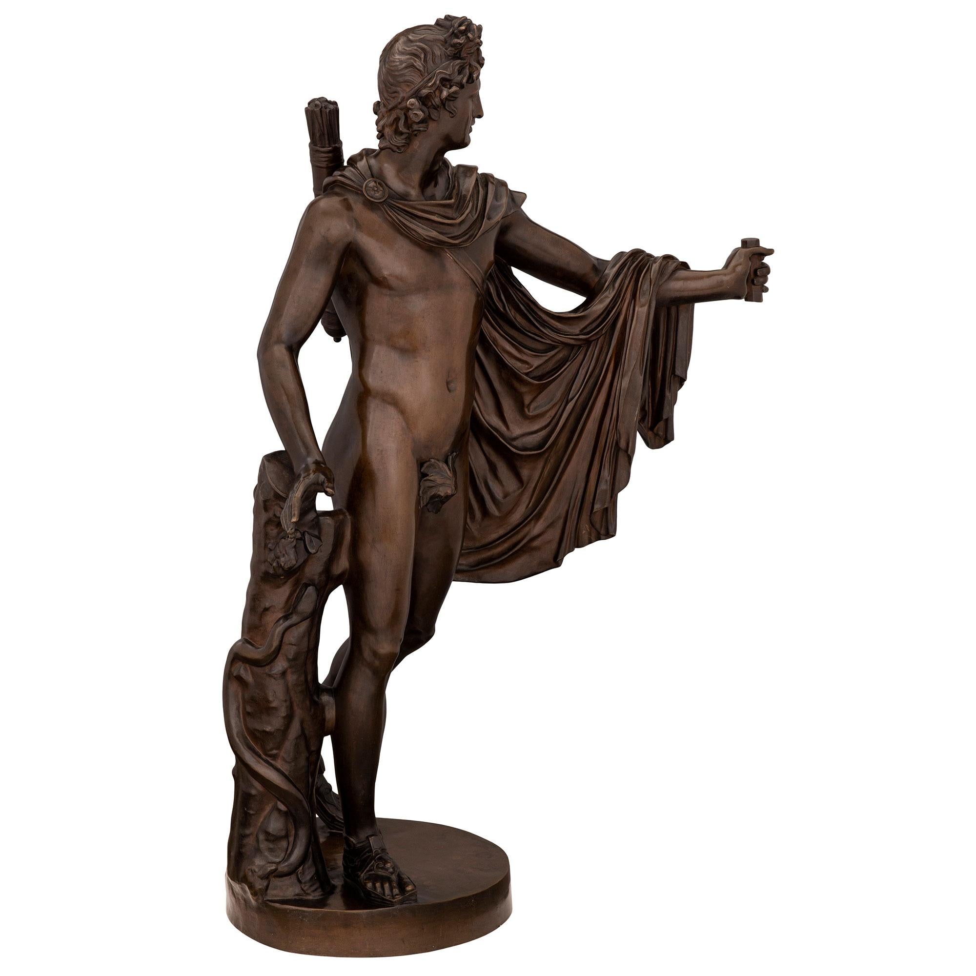 Belle statue d'Apollon en bronze patiné du XIXe siècle, signée F. Barbedienne, Fondeur. La statue est surélevée par une base circulaire avec un tronc d'arbre finement détaillé. Le bel Apollon est drapé dans une cape attachée autour de son cou et