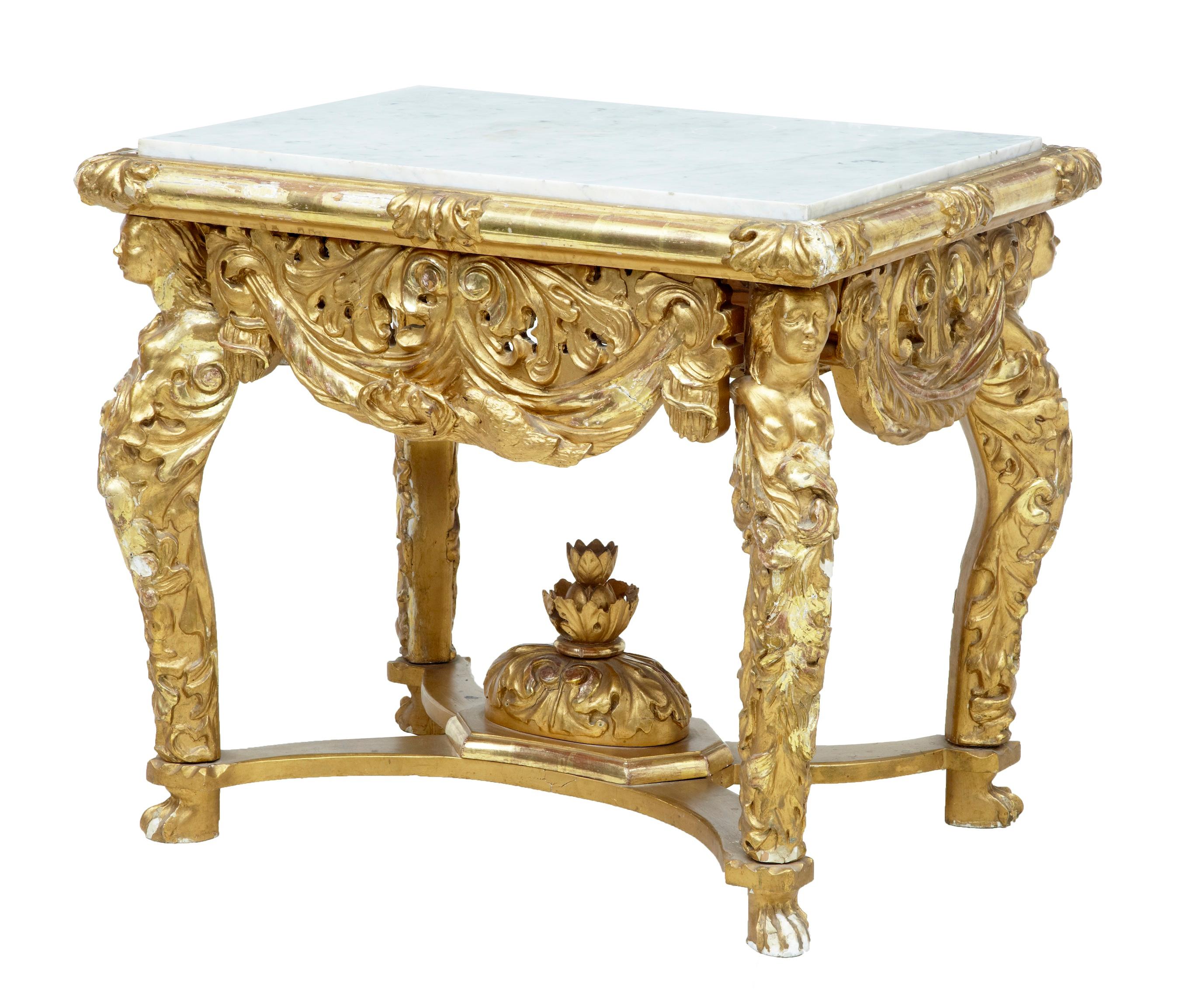 19th century carved wood and gilt center table, possibly italian. Circa 1850. Inset marble white grey veined top. Sides adorned with swags and scrolls.>each leg with carved female bust, with flowing acanthus leaves. Central decoration located in the