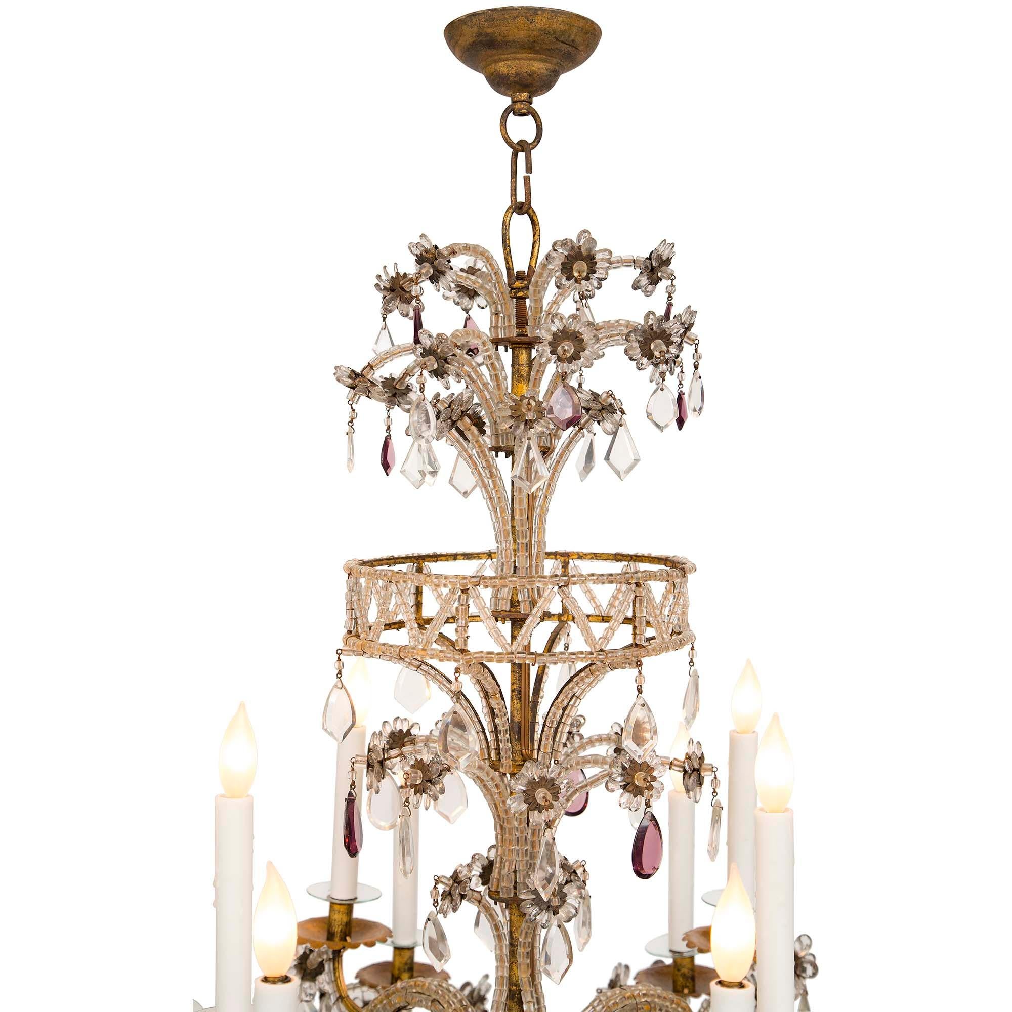 An elegant Italian 19th century gilt metal, crystal and glass twelve arm chandelier. The chandelier is centered by a solid crystal bottom ball amidst striking cut clear and violet colored crystals. Each of the finely scrolled arms are adorned with
