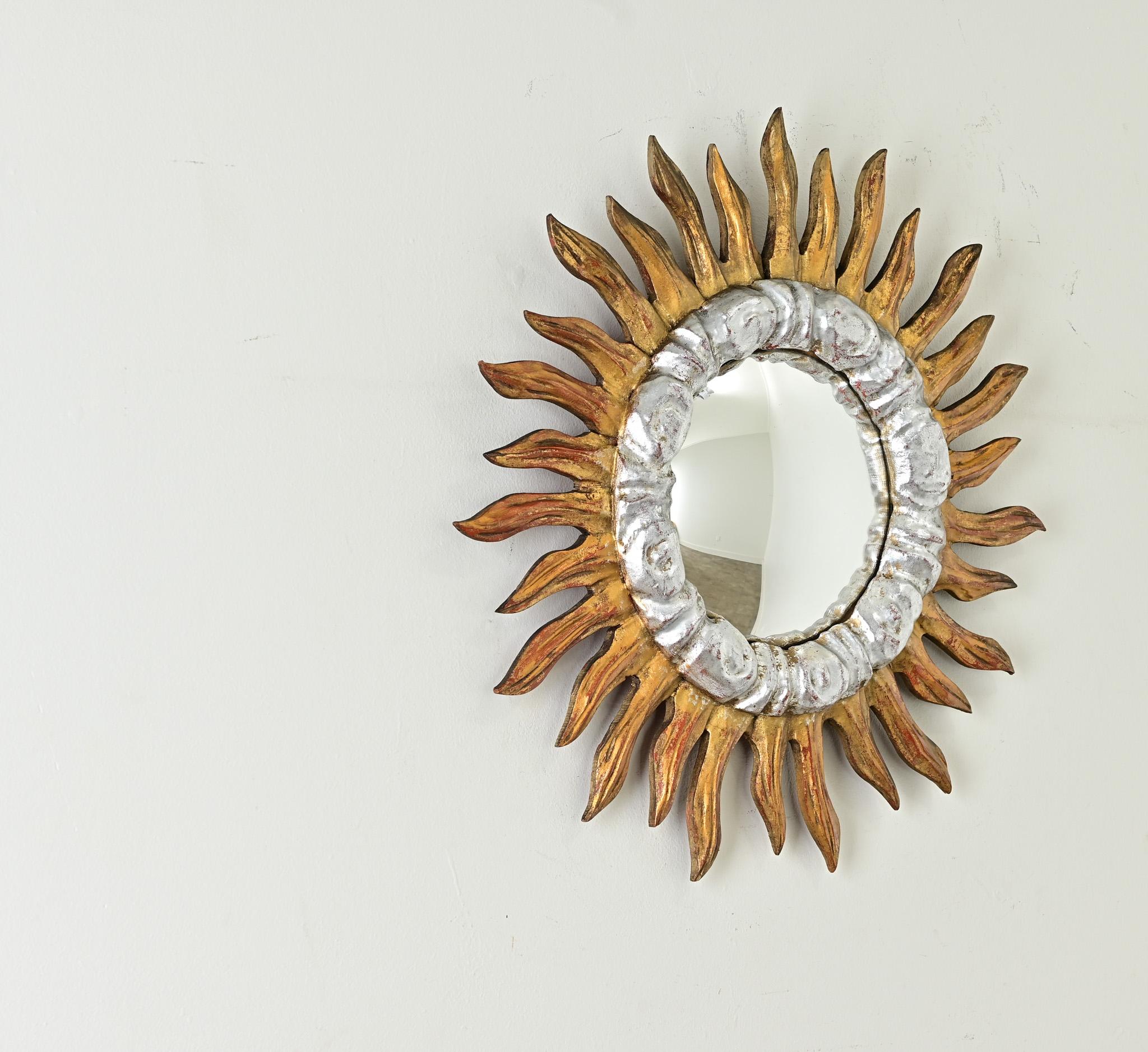 Ce miroir convexe en forme d'étoile possède une énergie indéniable qui illumine une pièce. La tige rouge exposée met en valeur la couronne de bois doré ardente qui semble danser autour de nuages de tourbillons dorés à l'argent. Un crochet à œil et