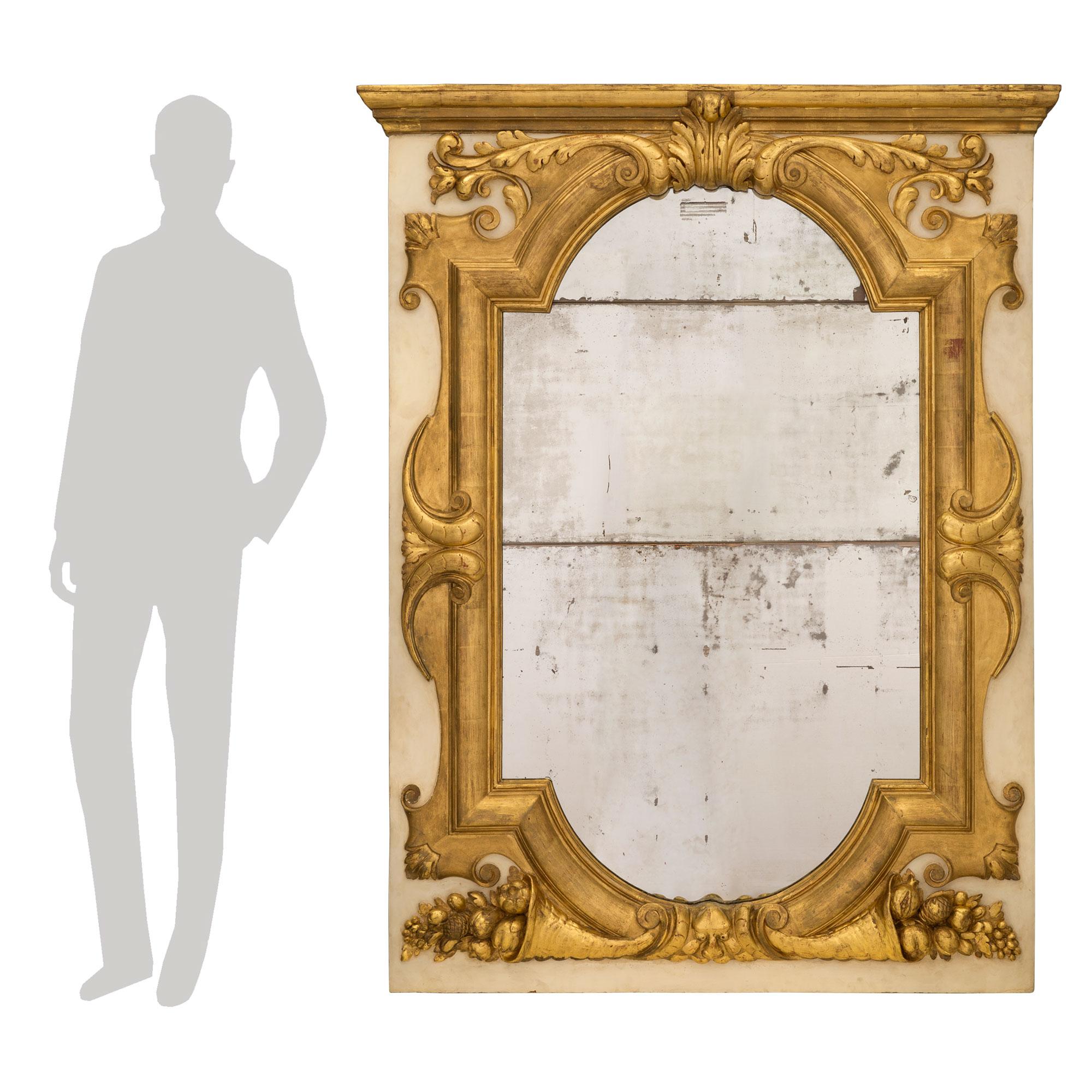 Un puissant miroir italien du XIXe siècle en bois doré et blanc cassé patiné. La plaque de miroir originale est entourée d'une impressionnante et très décorative bordure en bois doré moucheté sur un fond patiné blanc cassé. À la base, on trouve des