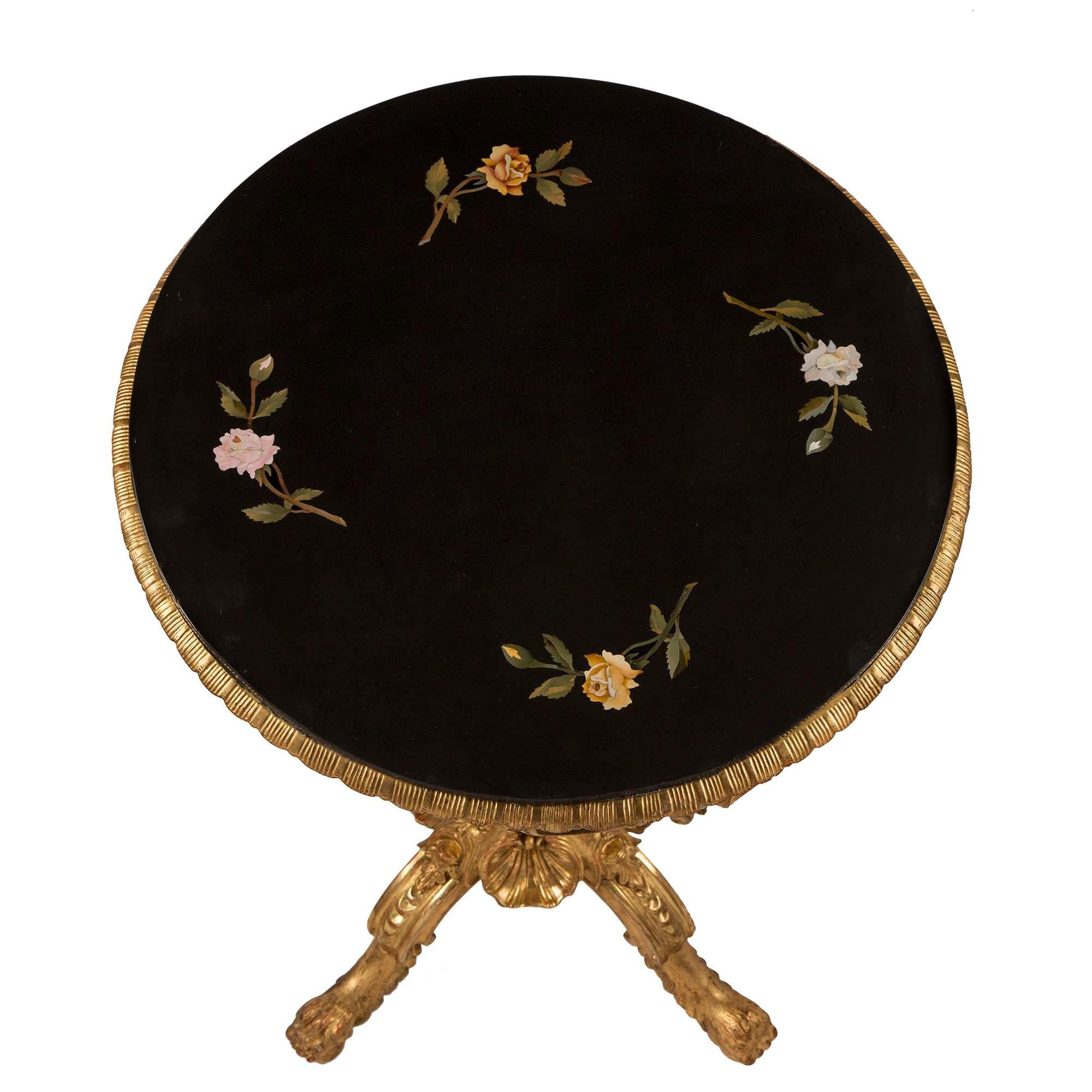 Charmante table d'appoint italienne du XIXe siècle en bois doré et marbre Pietra Dura. La table repose sur quatre pieds à volutes avec des motifs de pattes. À la base, de grands masques de théâtre sont placés sous le fut central. La frise de la