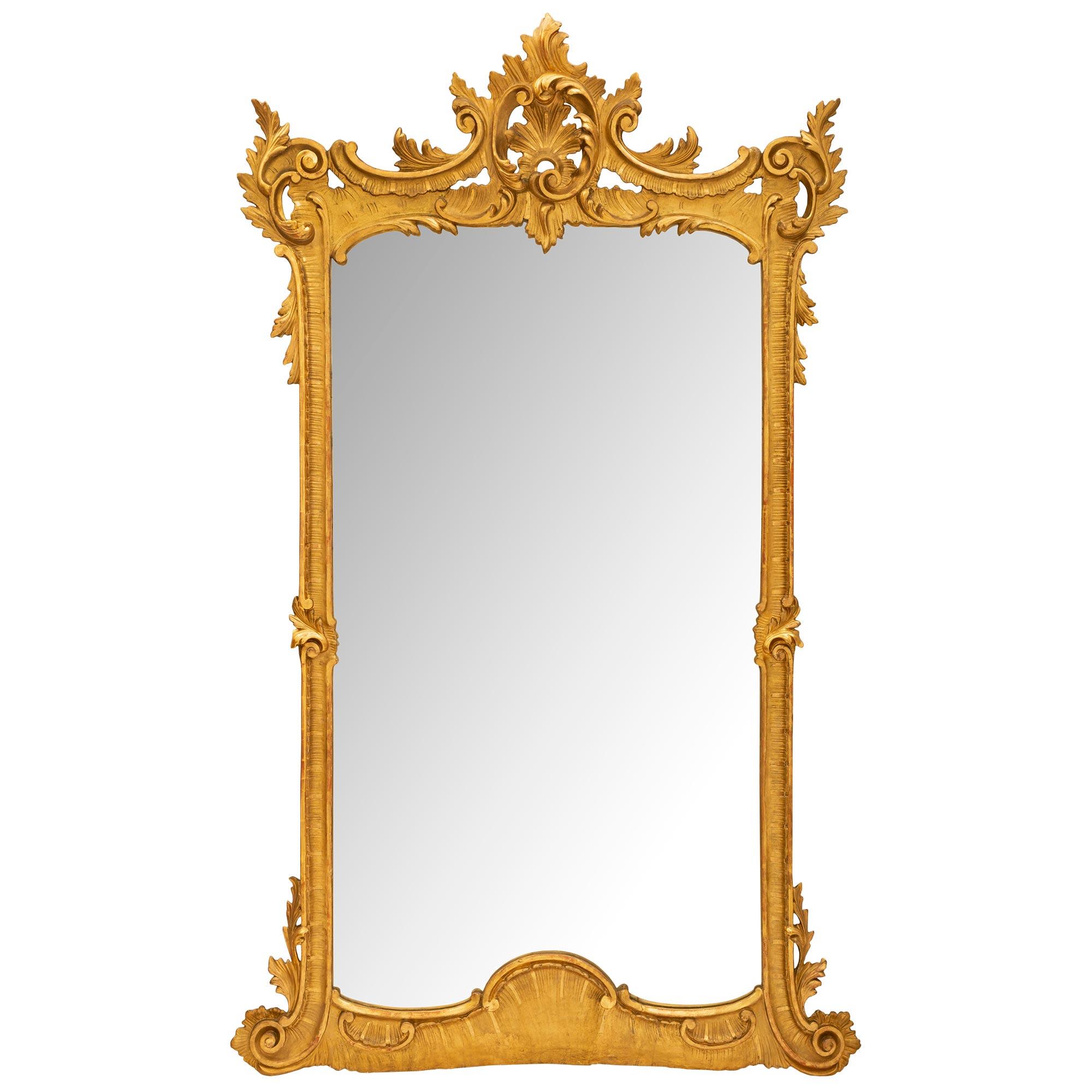 A beautiful mid 19th century Italian giltwood mirror with a satin and burnished finish. The mirror has 'S' scrolls at the bottom accented with acanthus leaves and a wide bottom border with a central shell design. At the top is a pierced central