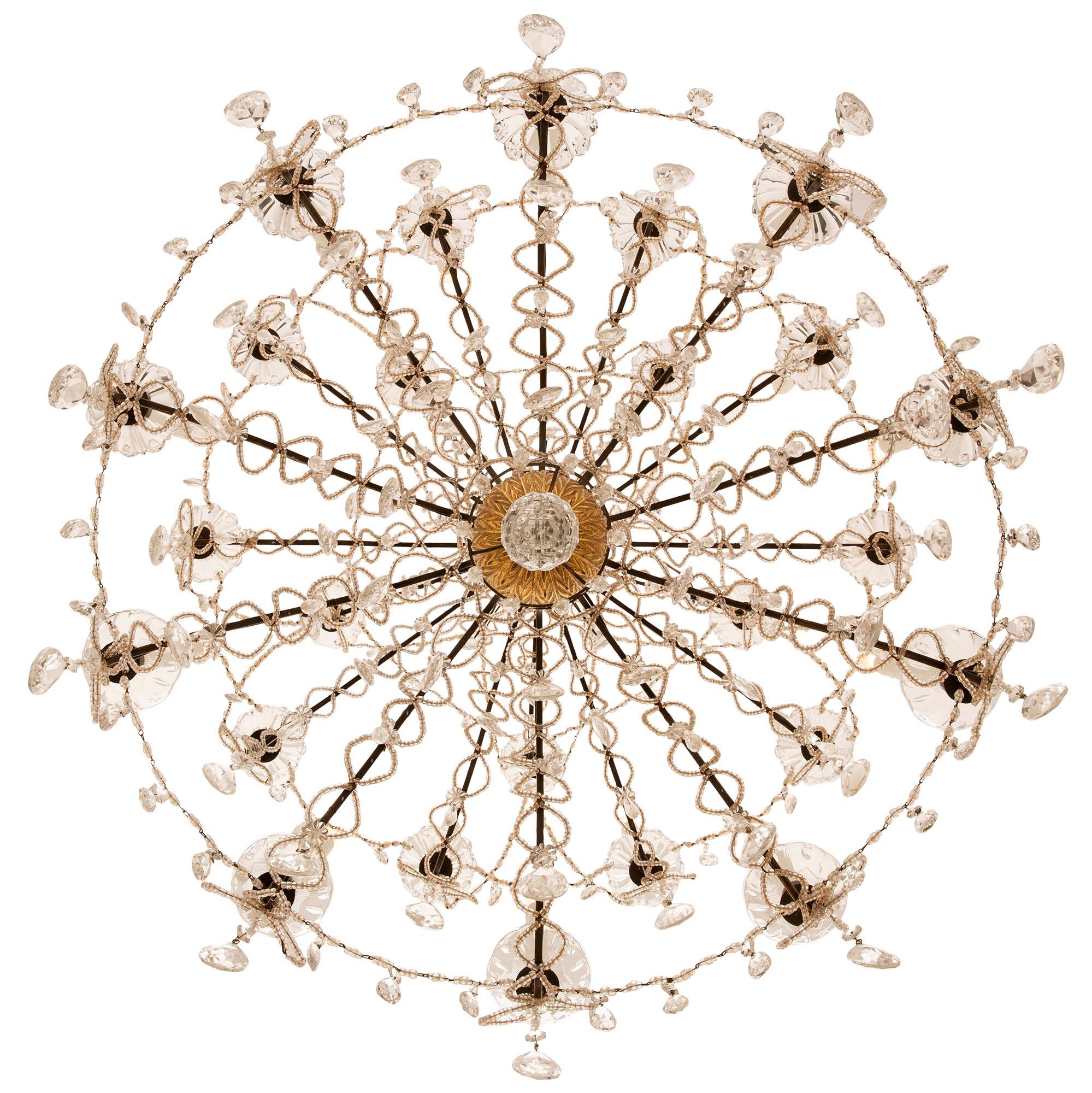A most elegant and large scaled Italian early 19th century Giltwood, patinated wood, Iron and Crystal chandelier. The three tier twenty five arm chandelier is centered by a stunning faceted crystal ball surrounded by prism shaped cut crystal
