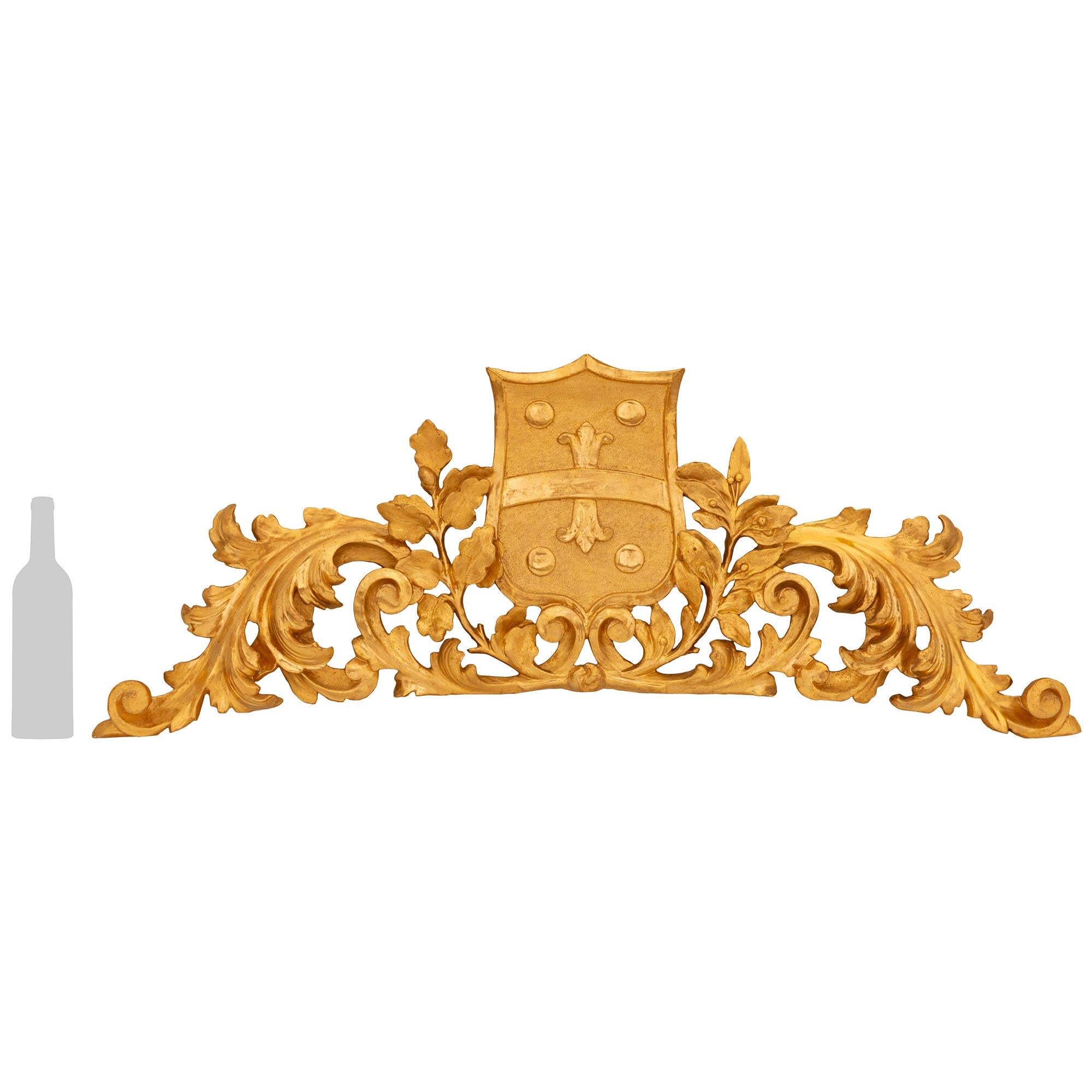A decorative and richly detailed Italian 19th century Giltwood wall decor/plaque. This stunning plaque displays a central crest with smooth and burnished cabochons at each corner with a band accented by a Fleur de Lys. The crest is flanked by finely