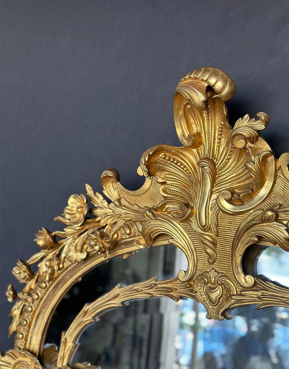 Elegant mirror in hand-carved gilded wood with botanical details that intertwine with two mythical looking creatures on each side. Beveled with 1