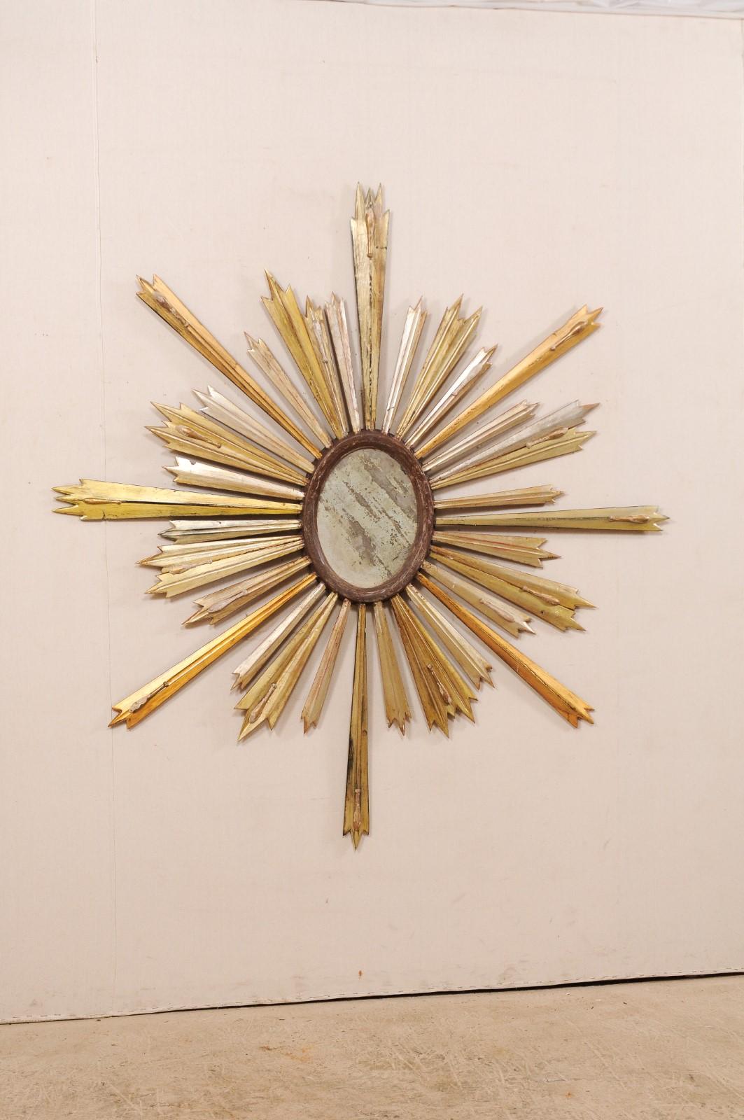An Italian gilded wood sunburst with mirrored center from the 19th century. This antique wall decoration from Italy features an oval-shaped central mirror within a wooden surround, from which gilded rays extend outward in various lengths resulting