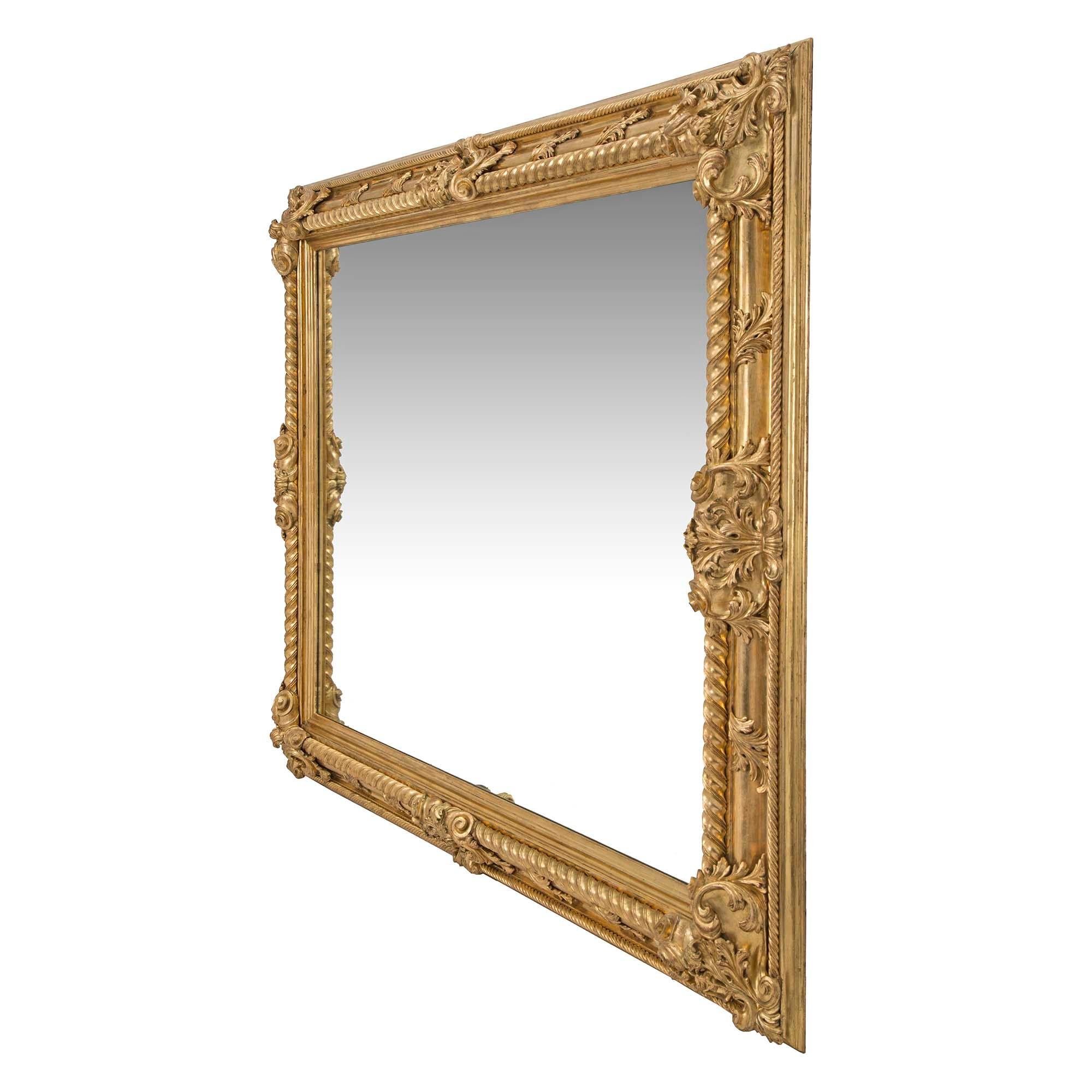 Miroir rectangulaire en bois doré de grande taille, de style Louis XIV, datant du XIXe siècle. Le miroir finement sculpté présente une bordure intérieure et extérieure en ruban torsadé, accentuée à chaque coin et sur les côtés par des motifs de