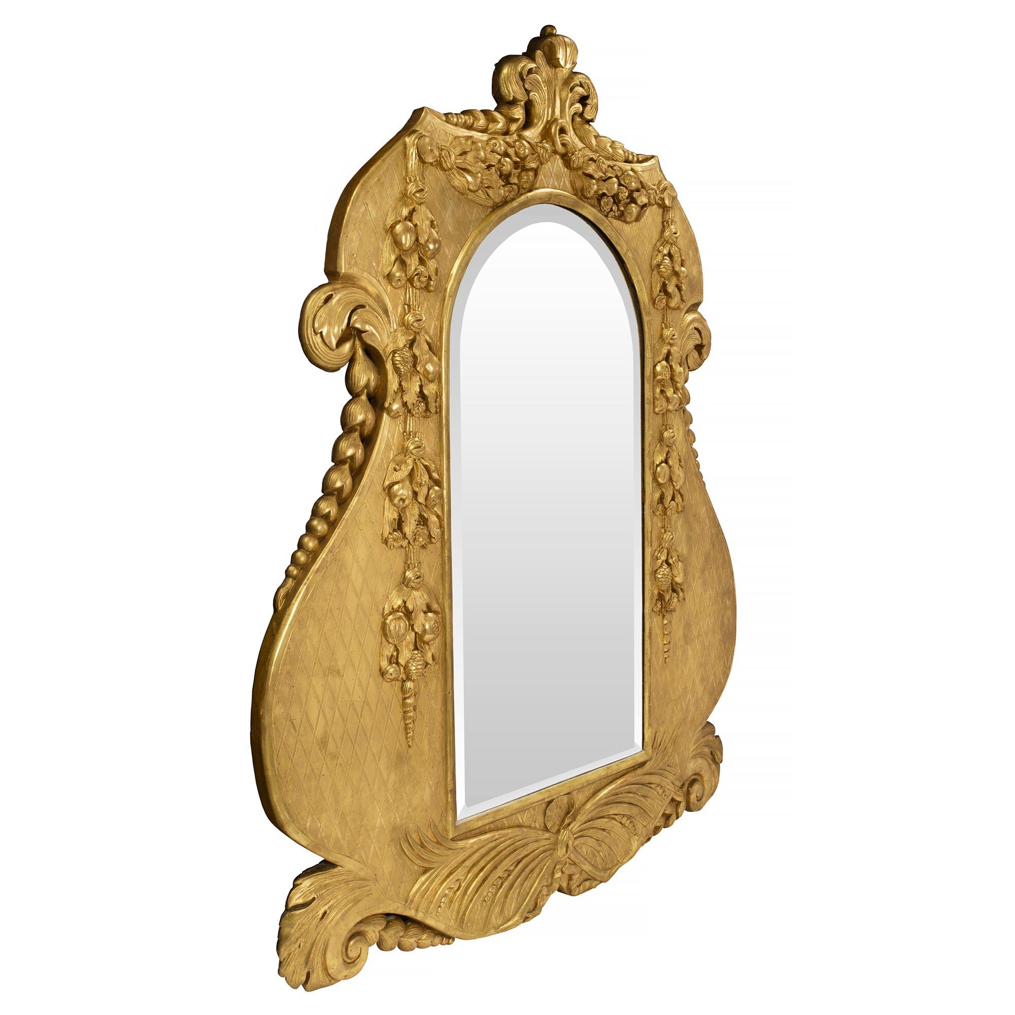 Impresionante y muy singular espejo italiano de madera dorada del siglo XIX, estilo Luis XV / Luis XVI. La placa original de espejo biselado está enmarcada en un encantador borde de madera dorada de forma inusual. El borde muestra un hermoso diseño