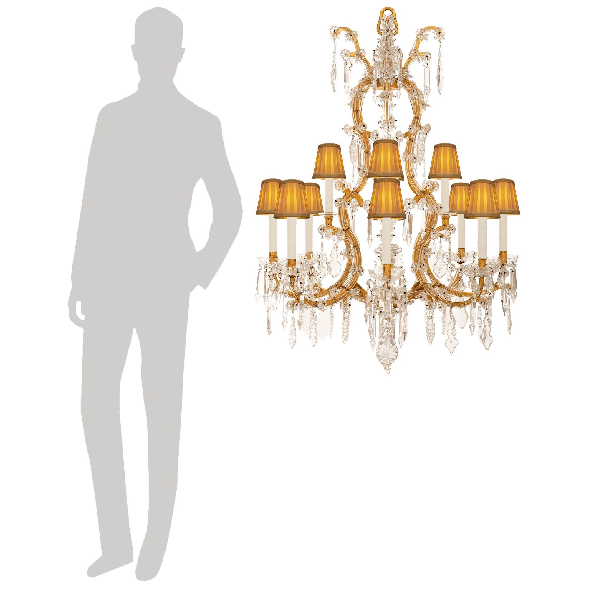 Un superbe et très élégant lustre italien du XIXe siècle de style Louis XV en fer doré, cristal et verre. Ce lustre exceptionnel à douze lumières est centré par un épi de faîtage en verre bérusé suspendu au centre du cadre en fer doré. Partant de la