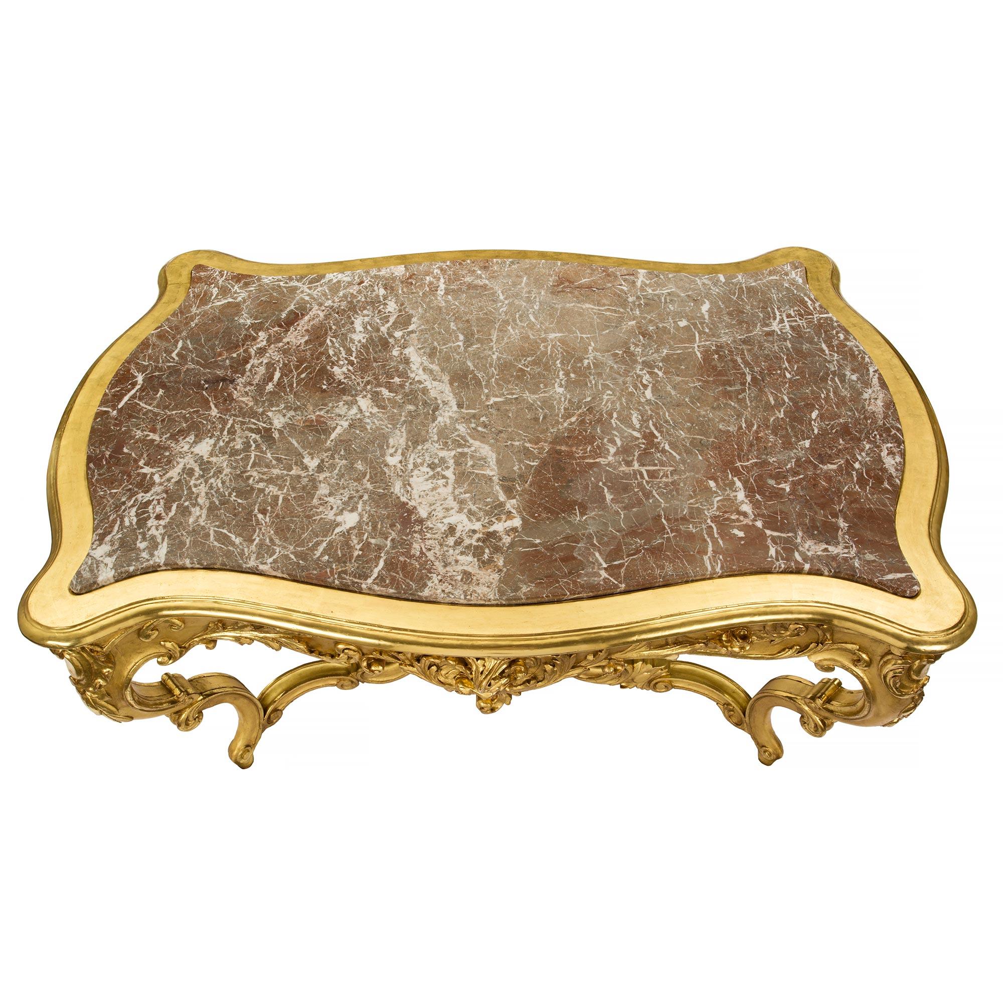 A sensational Italian 19th century Louis XV st. giltwood and marble center table with one drawer. The table is raised by exceptional scrolled legs with foliate movements and a most impressive elaborately carved central stretcher. Above each leg are