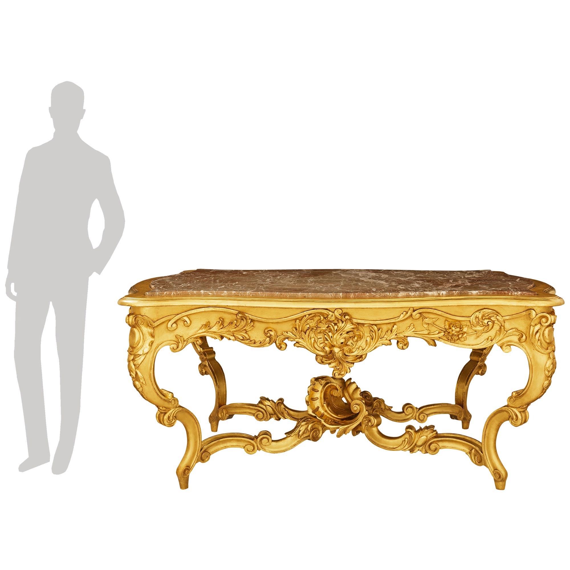 Sensacional mesa de centro italiana del siglo XIX de madera dorada y mármol de estilo Luis XV con un cajón. La mesa se eleva sobre excepcionales patas con volutas y movimientos foliados y una impresionante camilla central elaboradamente tallada.