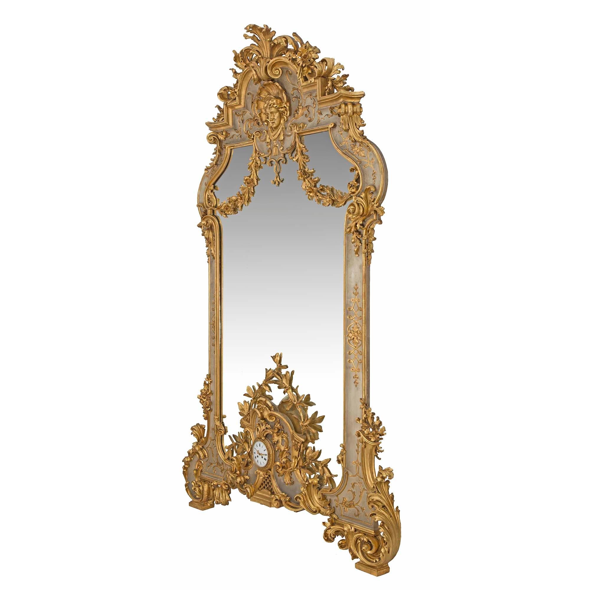 A monumental and extremely rare Italian mid 19th century Louis XV st. patinated and giltwood mirror with its own incorporated clock. Raised on giltwood feet with large opulent giltwood acanthus leaf scrolled at each side. Centered on the patinated
