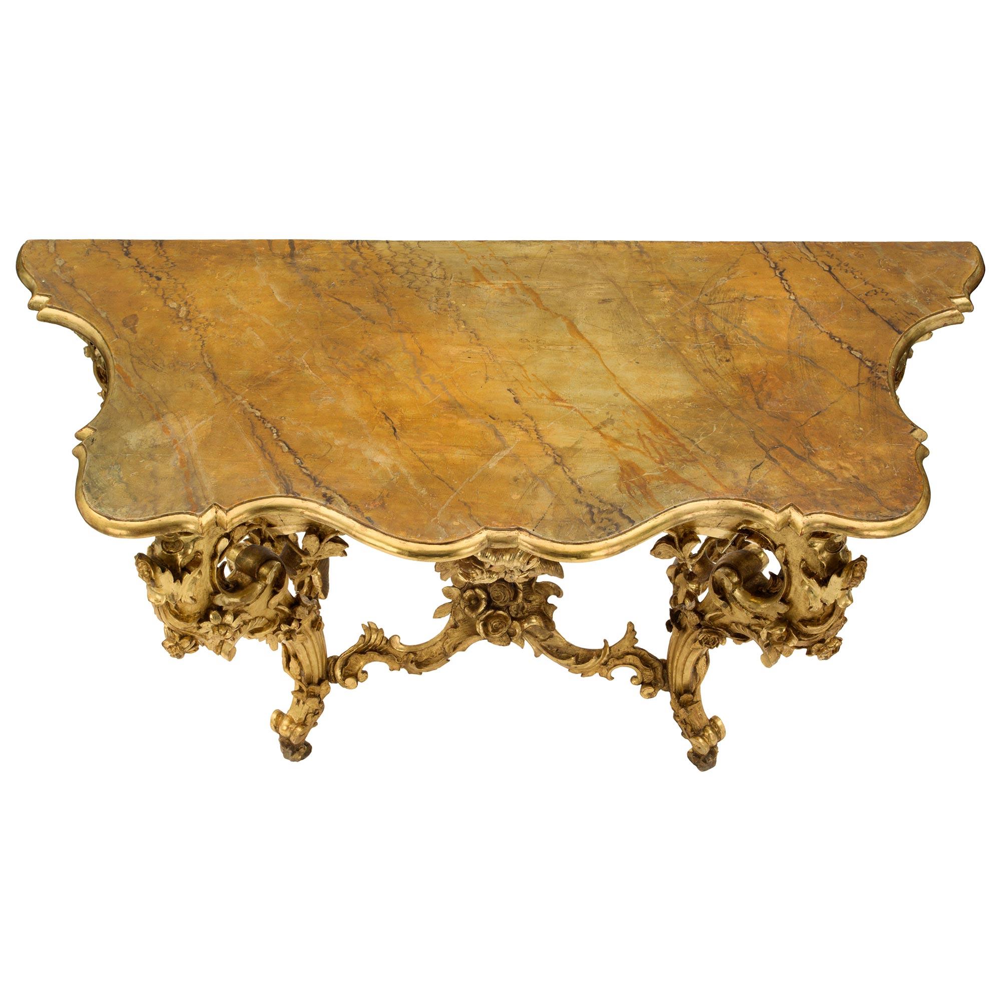 A stunning Italian 19th century Louis XV st. finely carved giltwood freestanding console. The impressive console is raised by S scrolled legs with exquisite elaborate foliate carvings of wrap around flowers and branches. Each leg is connected by the