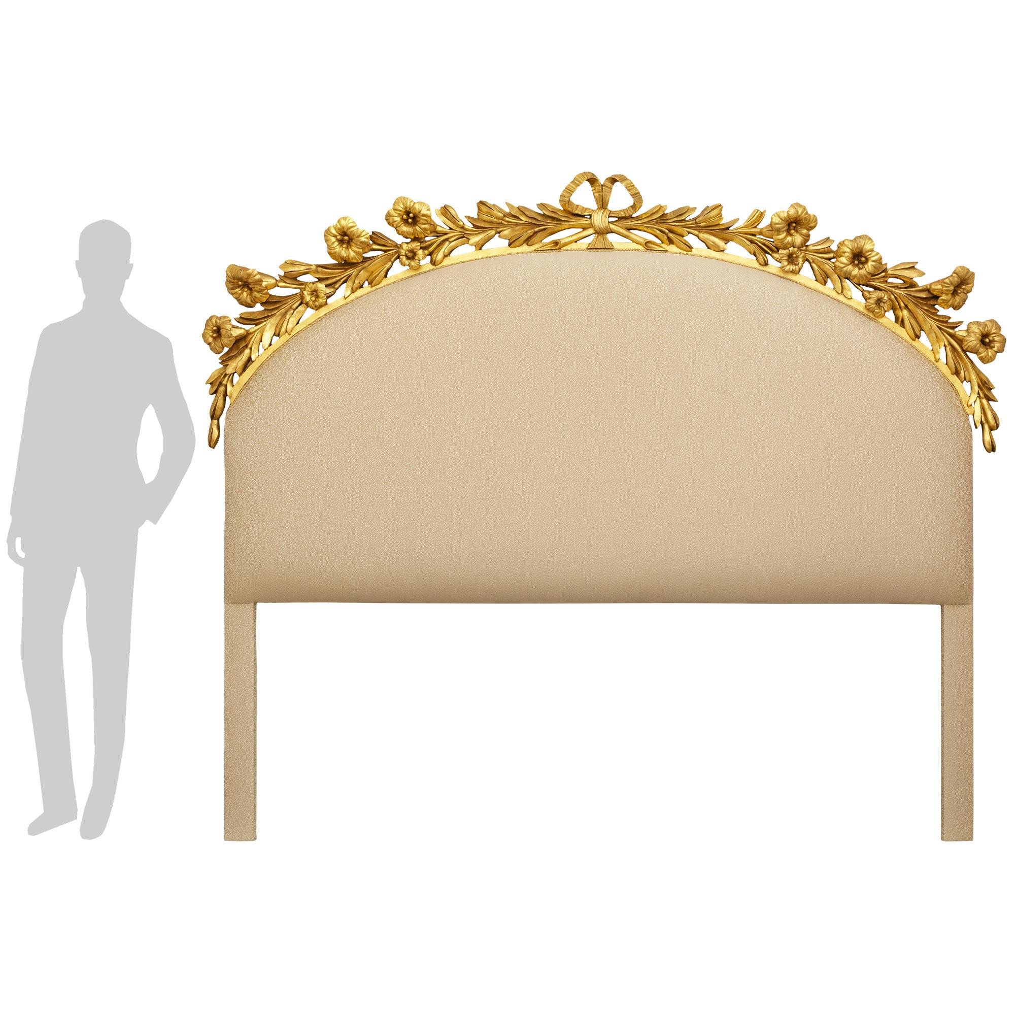 Une élégante et très décorative tête de lit king size en bois doré de style Louis XVI italien du XIXe siècle. Cette magnifique tête de lit rembourrée est richement décorée au sommet d'un nœud central en bois doré qui retient deux grandes branches