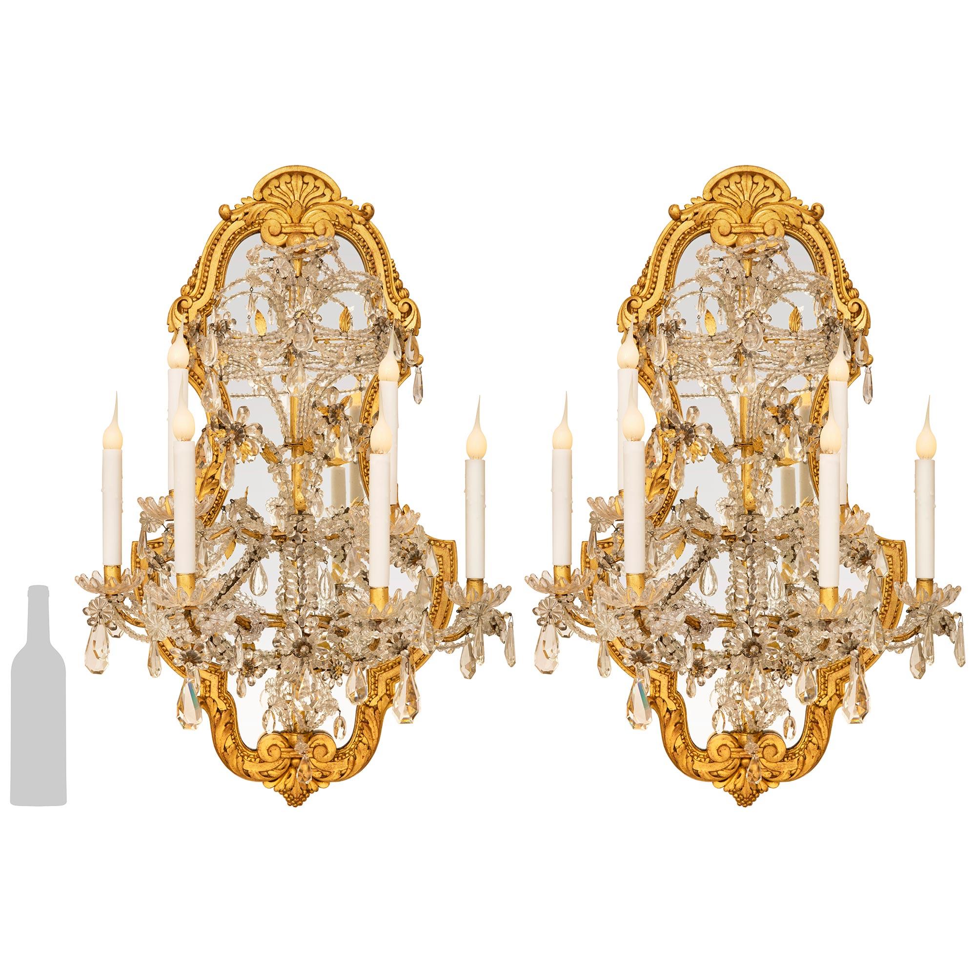 Impresionante pareja a gran escala de apliques italianos de madera dorada, espejo y cristal del siglo XIX, estilo Luis XVI. Cada candelabro de seis brazos está colocado sobre una maravillosa placa trasera de diseño foliado que muestra preciosos