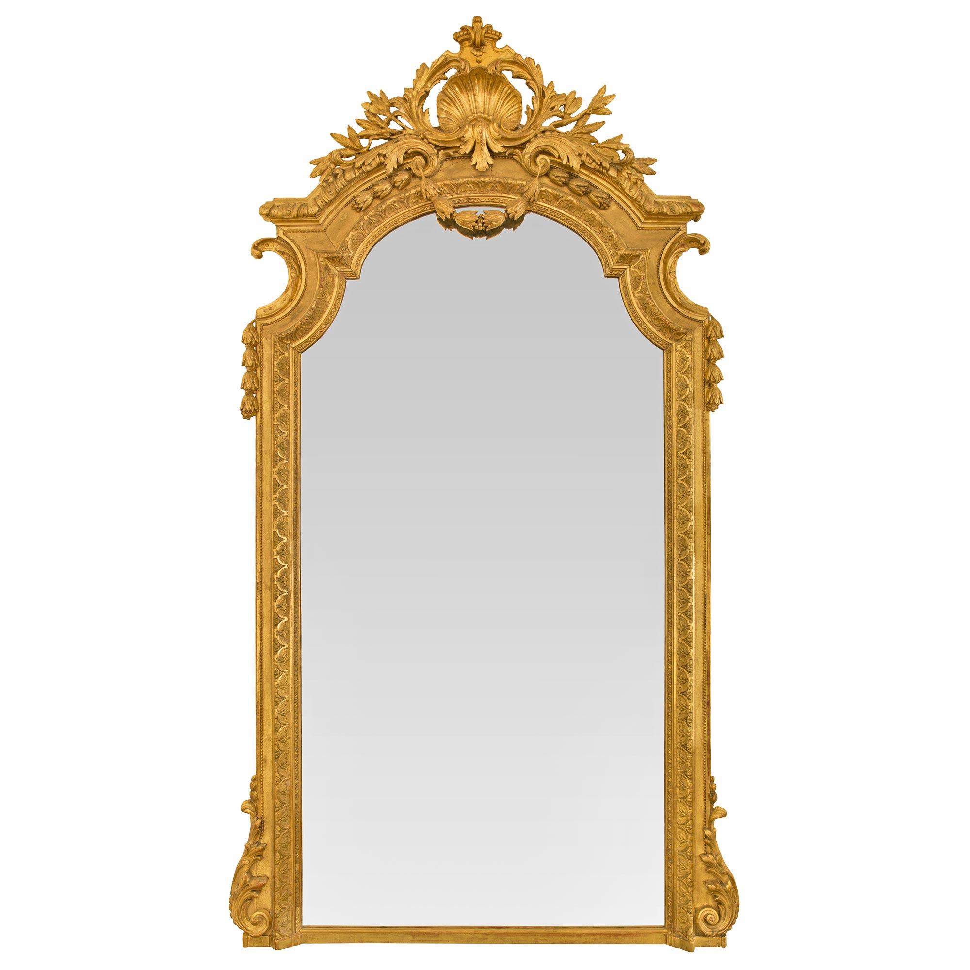 An impressive and large scale Italian 19th century Louis XVI st. giltwood mirror. The mirror displays an arched top with elegant lightly curved elements and is framed within a beautiful mottled border with a unique finely detailed sunburst like band