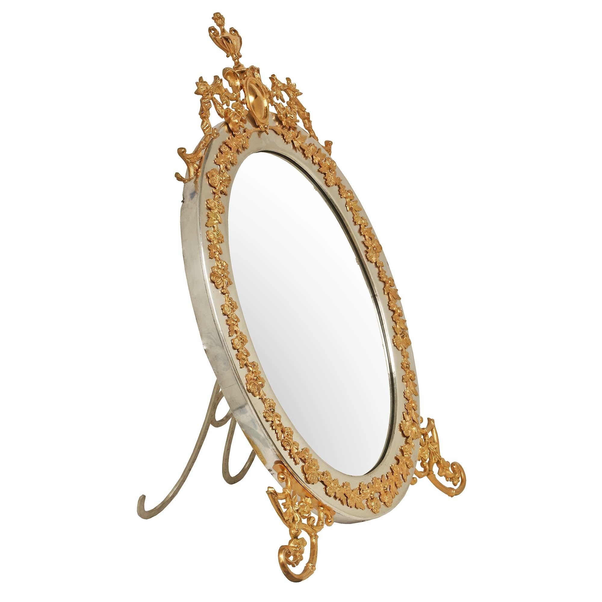 A unique and extremely elegant Italian 19th century Louis XVI st. ormolu and silvered bronze large scale lady's vanity mirror. The mirror is raised by two richly chased ormolu scrolled bamboo designed supports with foliate accents, and one fold out