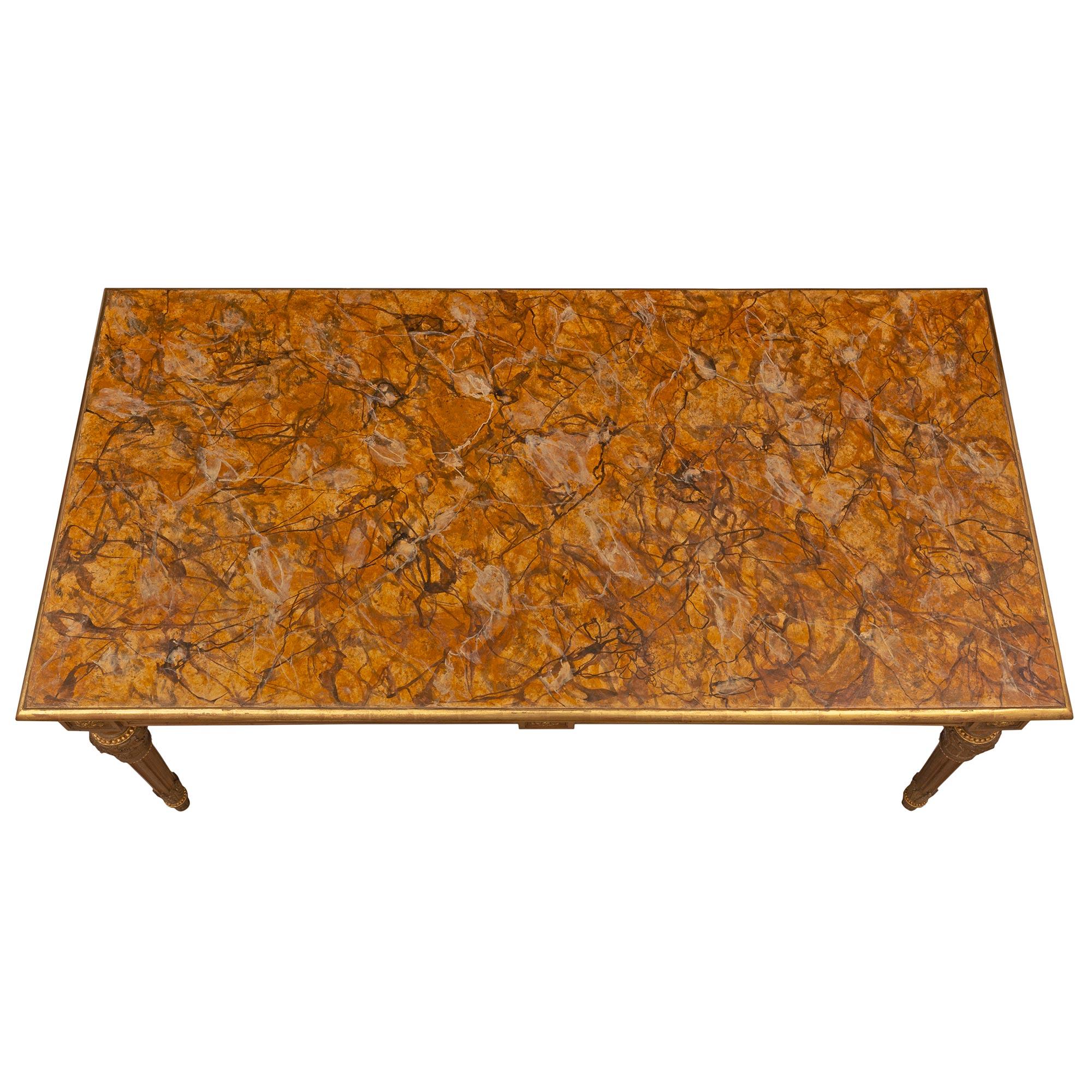 Elégante table centrale de style Louis XVI italien du XIXe siècle en noyer, bois doré et faux marbre peint. La table rectangulaire repose sur de fins pieds circulaires fuselés et cannelés, des pieds en forme de topie avec des bandes dorées