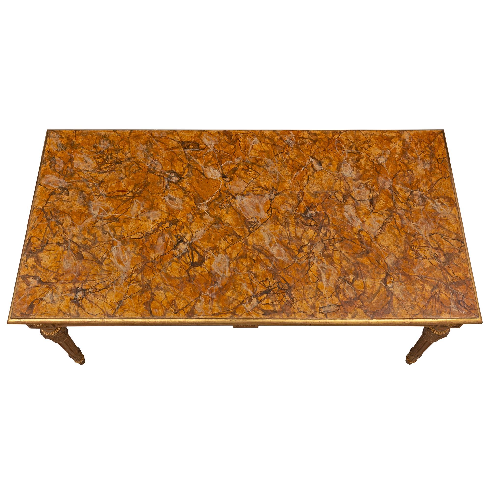 Élégante table centrale italienne de style Louis XVI du 19e siècle en noyer, bois doré et faux marbre peint. La table rectangulaire est surélevée par de fins pieds circulaires fuselés et cannelés, des pieds en forme de topie avec des bandes perlées