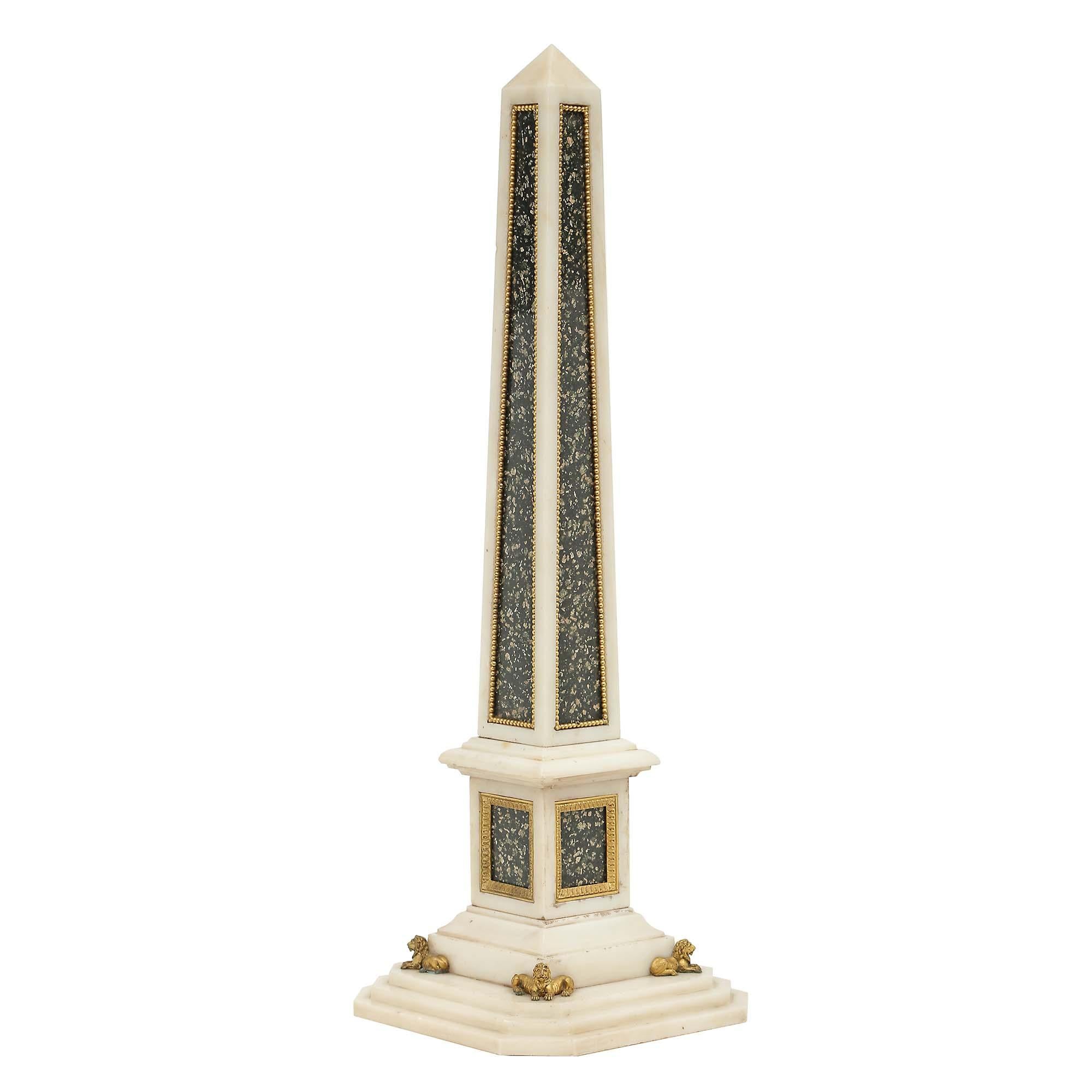 An impressive and very decorative Italian 19th century marble and ormolu obelisk. The handsome obelisk is raised on a square stepped white Carrara marble base with cut corners, accented with a finely chased ormolu lion at each corner. The obelisk