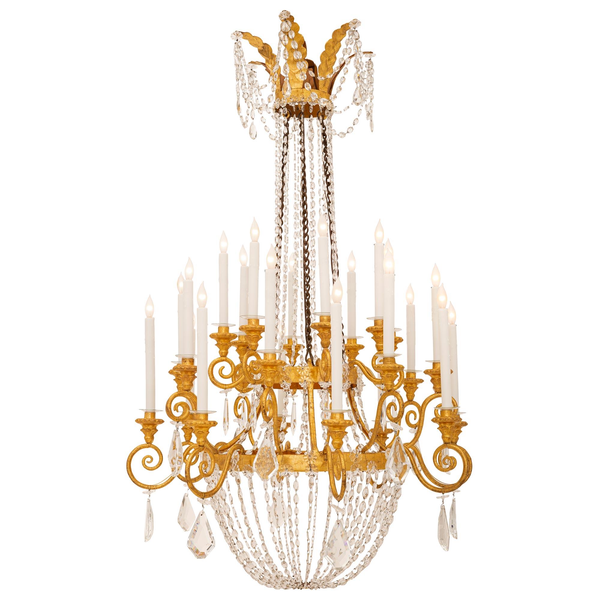 A stunning and large scale Italian 19th century Neo-Classical st. gilt metal, giltwood, iron and crystal chandelier. The twenty four arm chandelier is centered by a fine mottled bottom foliate reserve below an elegant array of lightly curved swaging