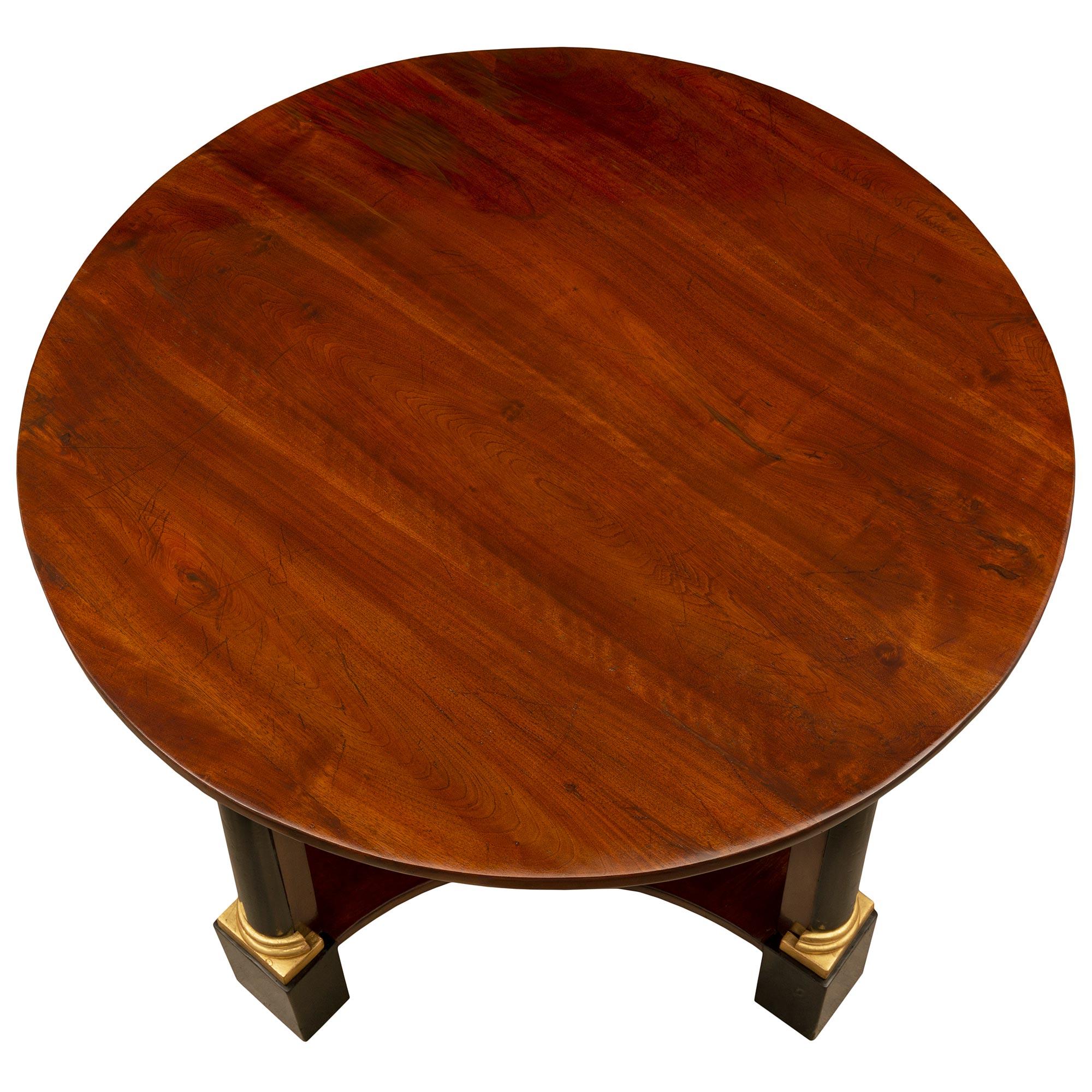 A handsome Italian 19th century Neo-Classical st. Mahogany, ebonized Fruitwood, and giltwood center table. The circular center table is raised by striking ebonized Fruitwood block feet below impressive column supports with mottled giltwood plinths