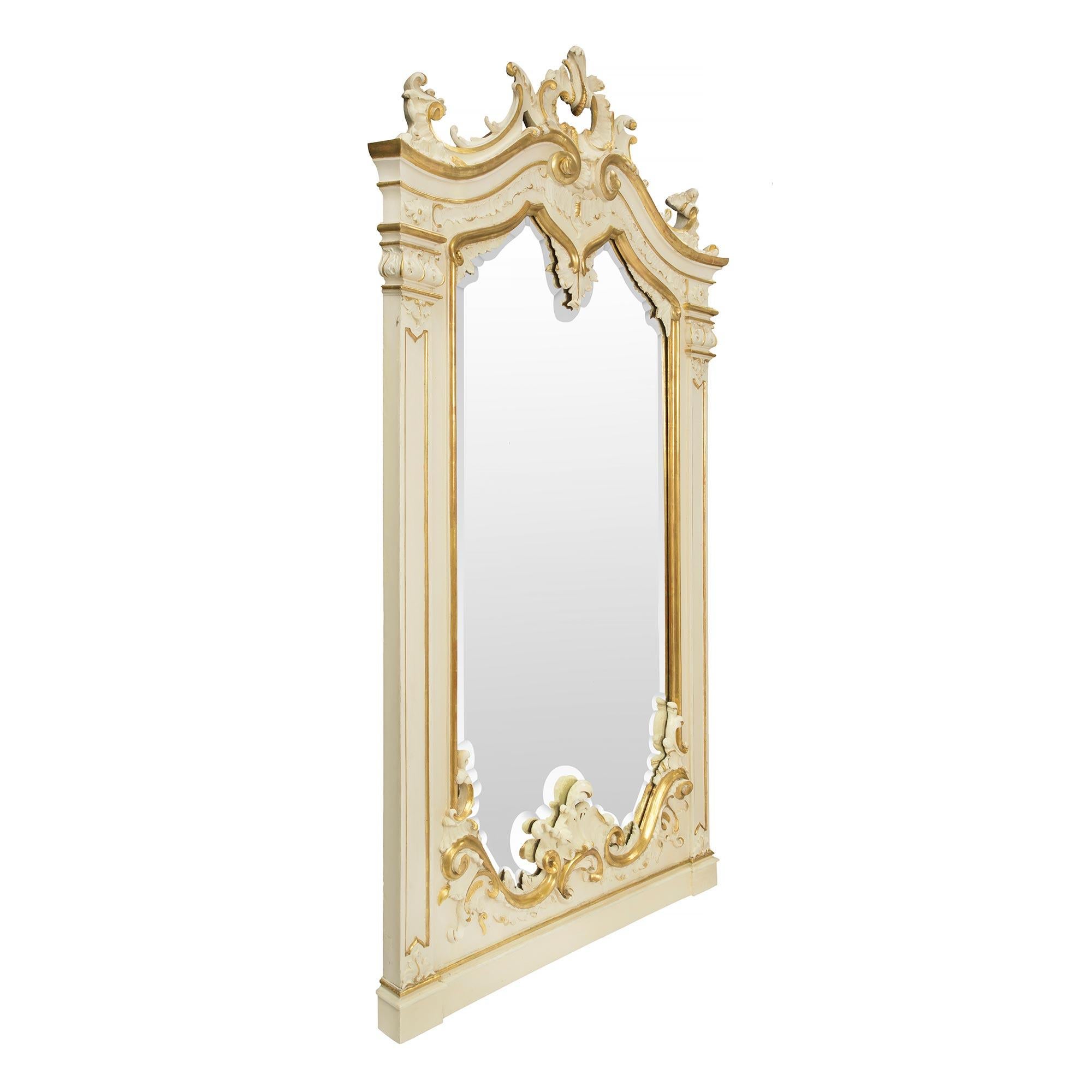 Un sensationnel et unique miroir vénitien italien du XIXe siècle, patiné et doré. Le miroir présente un bandeau inférieur marbré avec une impressionnante gerbe de feuillage sculptée au milieu de rinceaux dorés A.I.C. et C.C. Les deux panneaux