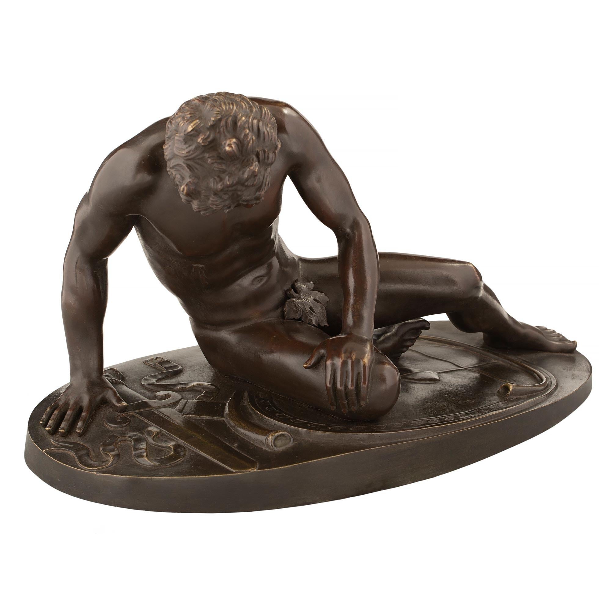 A handsome Italian 19th century patinated statue of 'The Dying Gaul'. The statue is raised by an oval shaped terrain like designed base. The fallen gladiator wears a neck tork, laying on his side and leaning on his arm. His sword and a horn are at