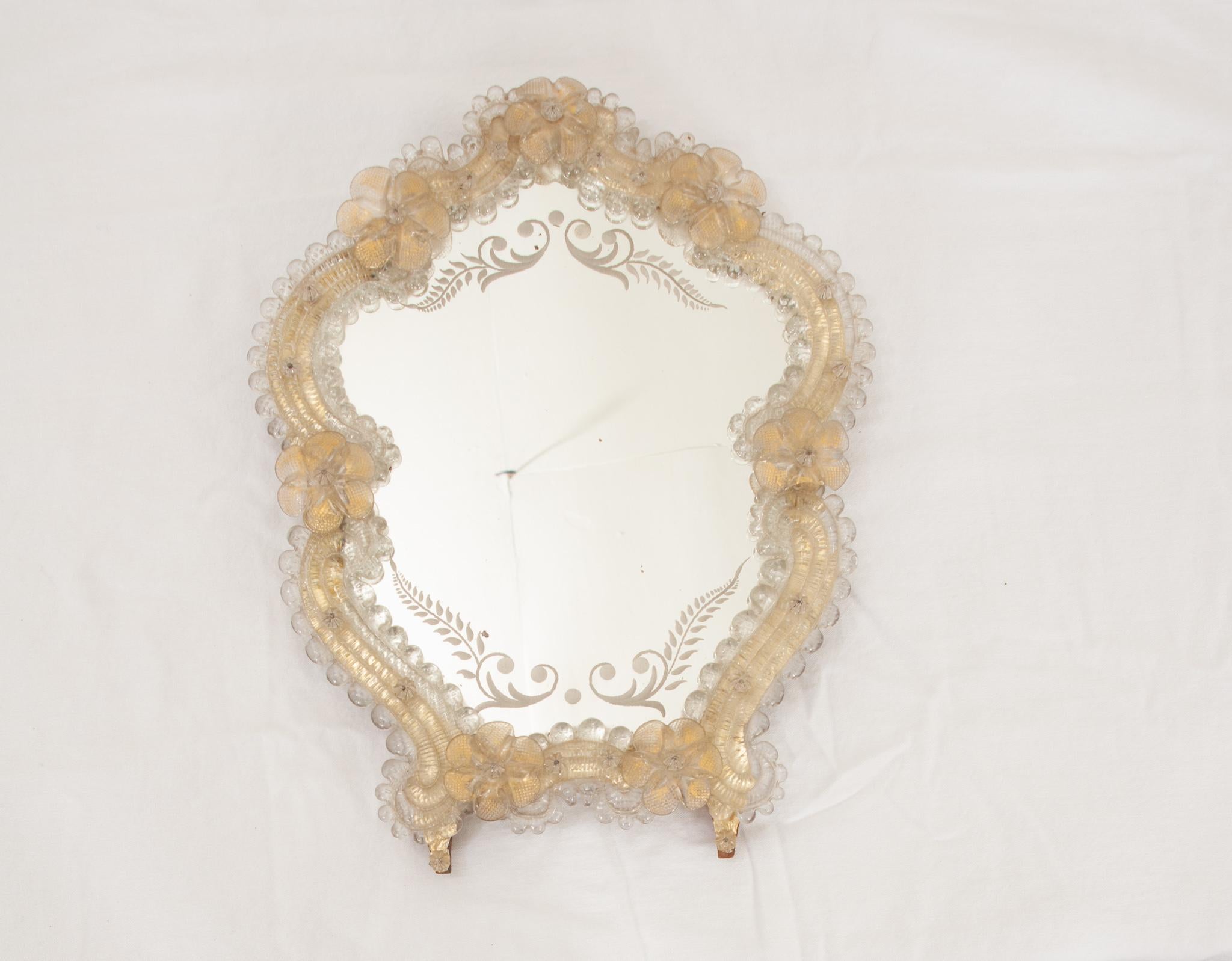 This diminutive mirror is a fabulous addition to any space. The antique mirror plate features beautiful fern inspired etchings on the top and bottom. Glass flowers dusted with gold gilt on their underside give off an glowing look. Fixed on a