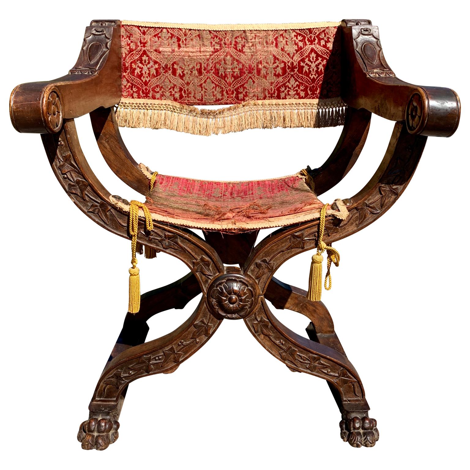 Fauteuil Dante italien du 19e siècle.
Magnifique fauteuil Savonarola en noyer avec une décoration ornementale sculptée. Cette imposante chaise à piètement en X est dotée d'un riche revêtement en velours, de franges dorées et d'assises gommées. Il