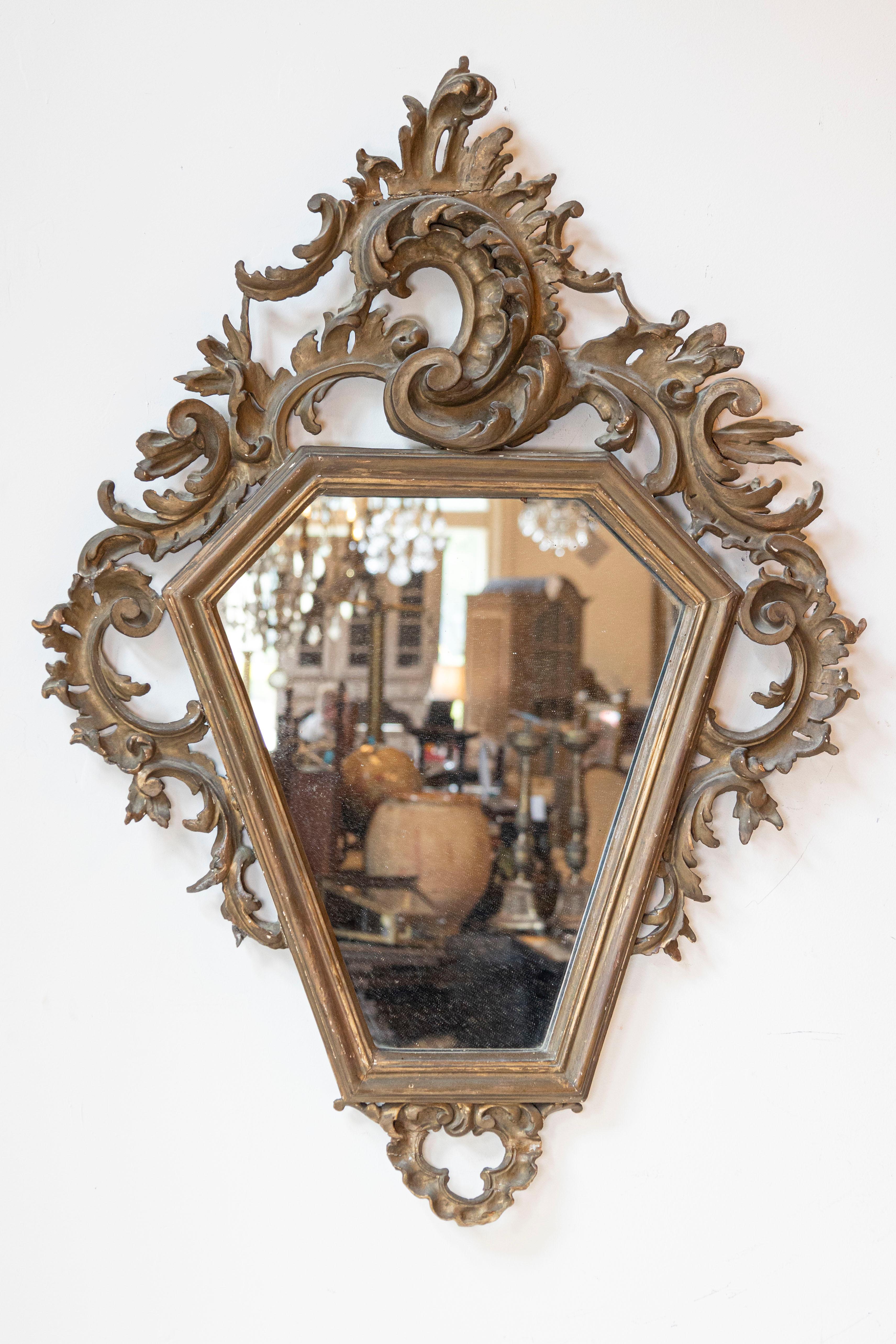 An Italian Rococo style carved mirror from the 19th century, with traces of gilt. Created in Italy during the 19th century, this piece features a polygonal mirror plate surrounded by an eye-catching carved frame showcasing Rocailles c-scrolls and