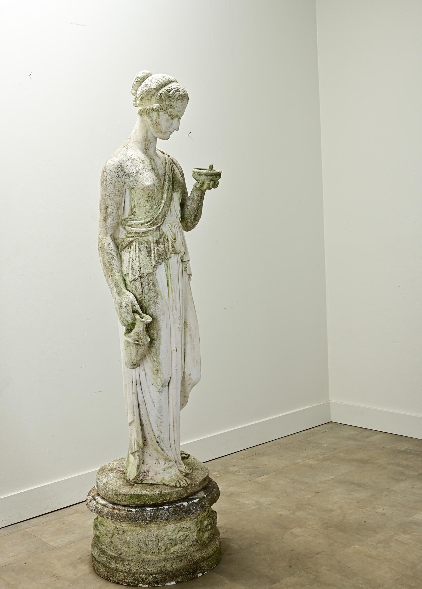 An Italian statue of Greek goddess, Hebe, signed by the artist, Andrea Parini, is lifted on a round pedestal base and made of portland cement. Hebe, the goddess of eternal youth, is the daughter of Hera and Zeus and the wife of Hercules in Greek