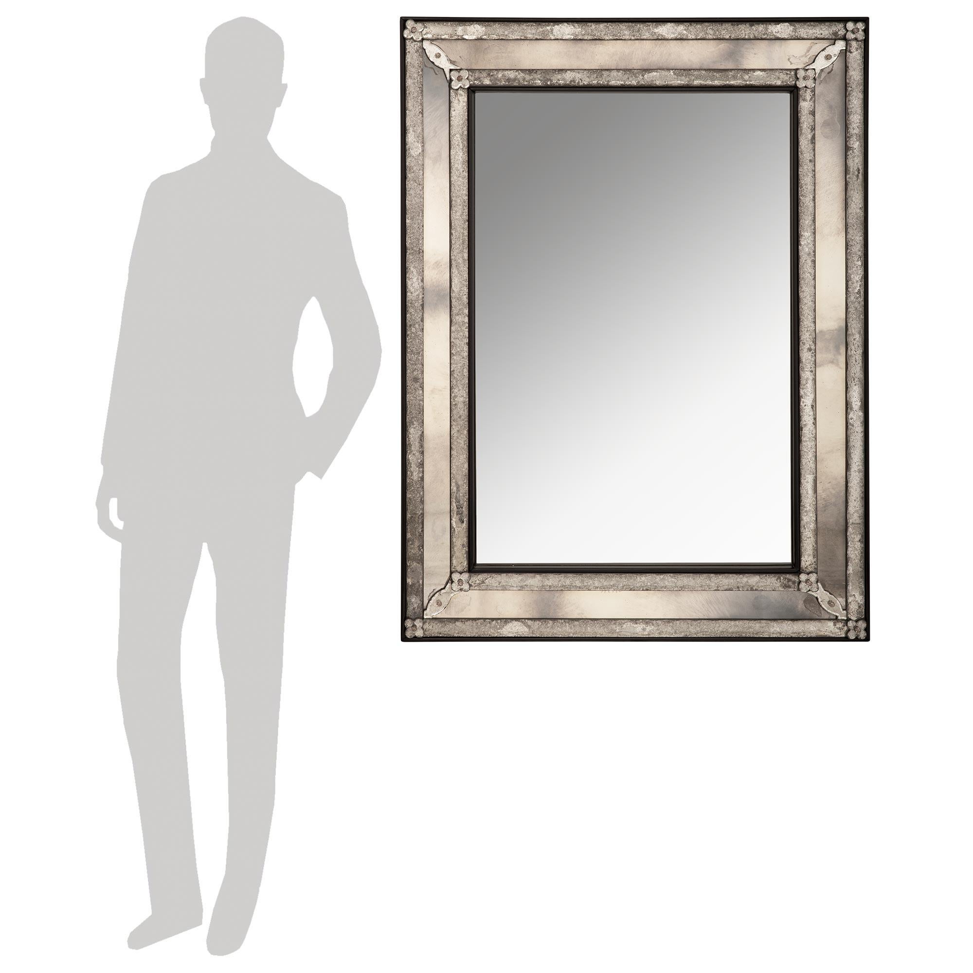 Un'imponente ed elegante specchiera veneziana del XIX secolo. Questo splendido specchio a doppia cornice presenta una cornice in ebano con dettagli raffinati. I quattro angoli sono decorati con gusto con rosette, mentre a separare le due piastre a