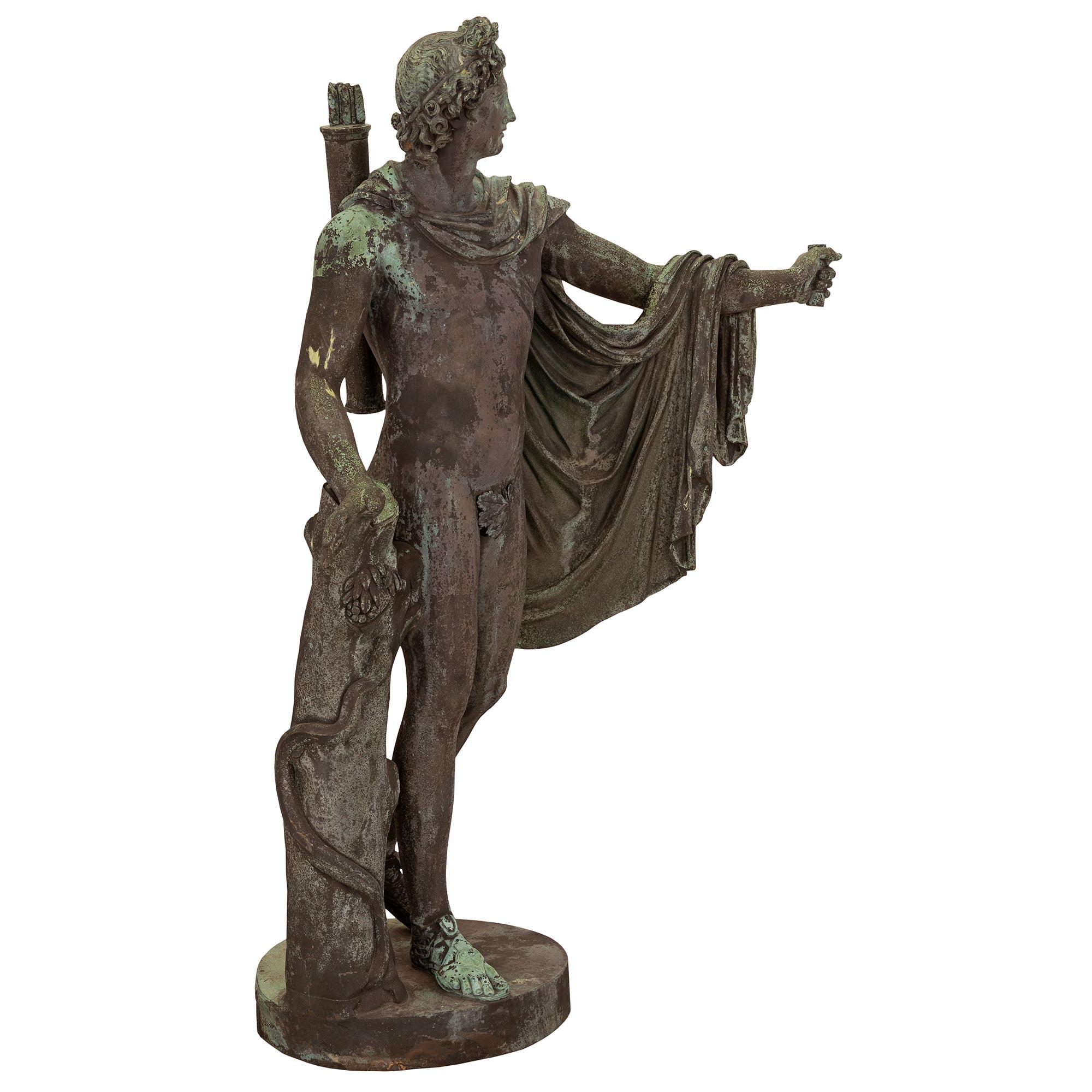 Belle statue italienne d'Apollo en bronze vert-de-gris du XIXe siècle, de grande qualité. La statue est surélevée par une base circulaire avec un tronc d'arbre finement détaillé. Le bel Apollo est drapé dans une cape attachée autour de son cou et